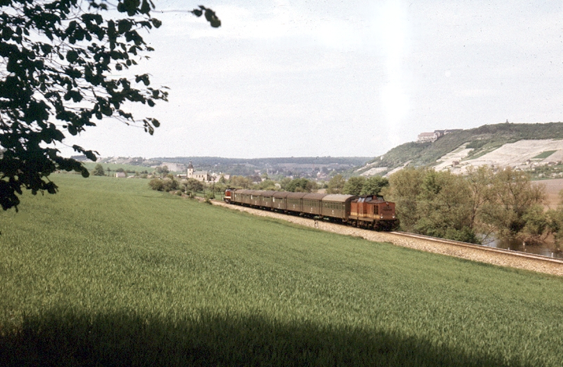 Ein Personenzug von Naumburg Hbf nach Nebra bzw. Artern mit jeweils einer V100 am Kopf und Ende des Zuges. Ab Nebra zieht die 112er den vorderen Zugteil weiter nach Artern und die 110er am Ende den anderen Zugteil zur�ck nach Naumburg Hbf. Bei der 112er handelt es sich um eine der sehr gepflegten  Garagenloks  vom Bw Sangerhausen. Klaus Pollm�cher fotografierte den Zug am 12.05.1986 im Unstruttal bei Ni�mitz.