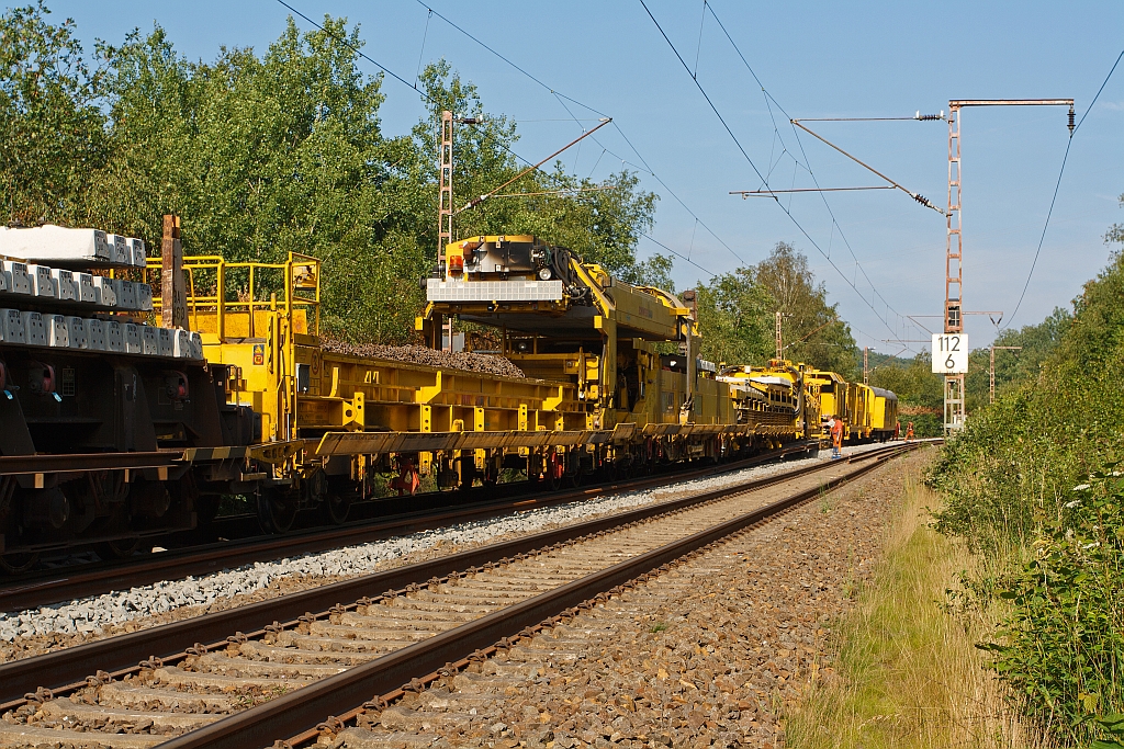 Schweizer Hightech auf der KBS 445 in Winsdorf-Anzhausen an 31.07.2011. Die zwei Schwellen-Portalkrane von dem MATISA Umbauzug P95 der Schweerbau bei der Arbeit.


Der Antrieb (500 KW Leistung) erfolgt im Arbeitsbetrieb auf 4 von 5 Drehgestelle hydrostatisch (hydraulisch), die max. Geschwindigkeit ist 5 km/h.


Die 2 Portalkrane haben jeweils einen eingen Dieselmotor, der Fahrantrieb erfolgt auch hydrostatisch.