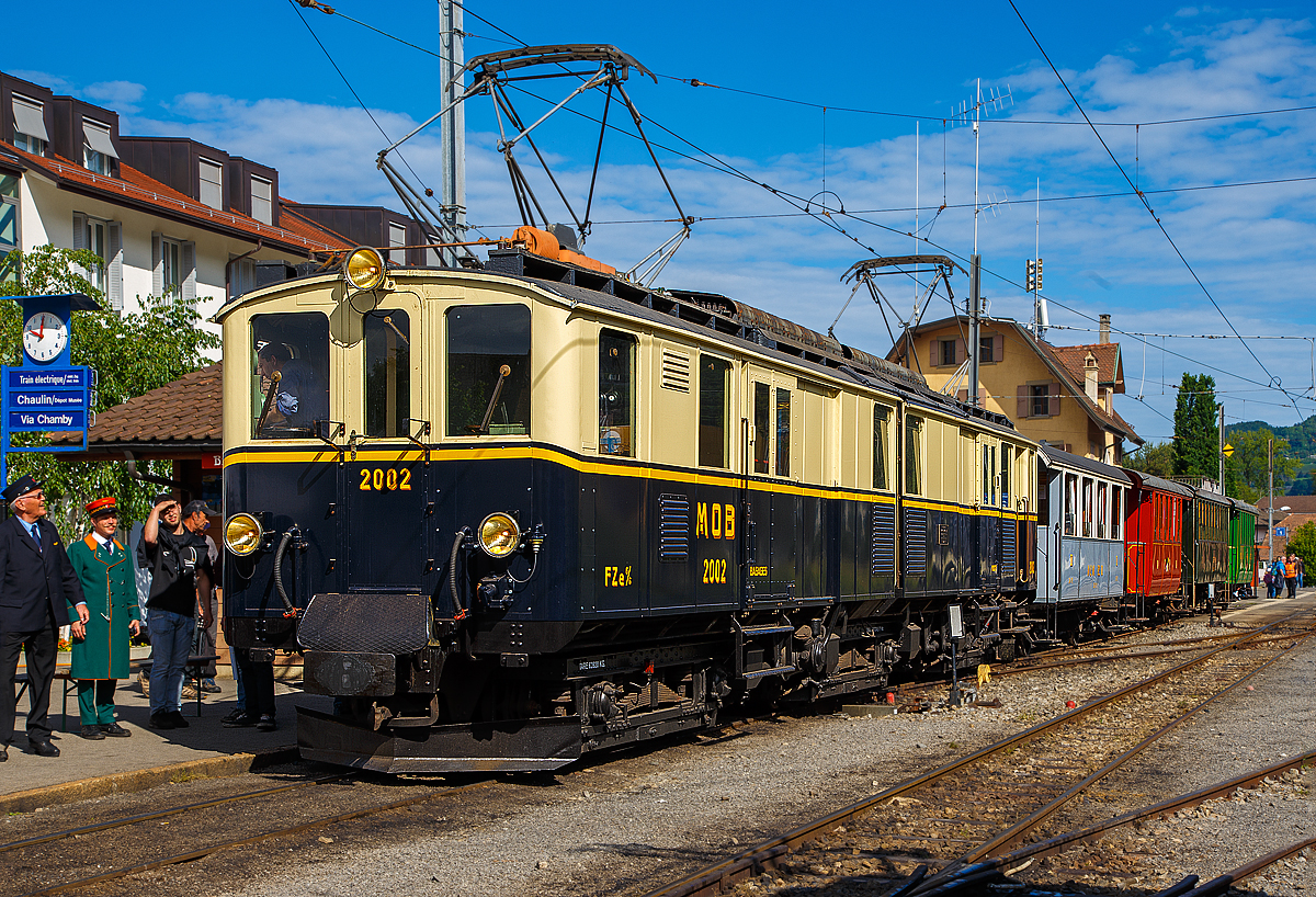 
50 Jahre BC - MEGA STEAM FESTIVAL der Museumsbahn Blonay–Chamby:
Bevor wir nach Vevey herunter „surften“...
Konnten wir noch im tollen Morgenlicht den wunderschöne Gelenktriebwagen ex MOB DZe 6/6 2002, bzw. FZe 6/6 2002 bestaunen und fotografieren. Hier steht er am 21.05.2018 im Bahnhof Blonay mit einem Zug zur Abfahrt zum Museum bereit.

Der Triebwagen Gepäck- und Postabteil wurde 1932 von SIG unter der Fabriknummer 3703 gebaut, der Elektrische Teil ist von BBC. Der Gepäcktriebwagen war bis 1996 im Einsatz und wurde dann in der Remise Gstaad Abgestellt und gammelte vor sich hin, bis er im Juli 2008 zur Museumsbahn Blonay–Chamby ging.

Die MOB (Montreux–Berner Oberland-Bahn) beschaffte für die Bespannung des “Golden Mountain Pullman Express” die beiden zweiteiligen Gelenktriebwagen FZe 6/6 2001 und 2002 (MOB-intern immer „Lokomotiven“ bzw. „Gepäcklokomotiven“ genannt). Nachdem der Expresszug schnell wieder eingestellt wurde (vor der Lieferung), fanden die beiden Gelenktriebwagen ein neues Betätigungsfeld im schweren Schnellzug- und Güterzugverkehr bzw. bespannten Sonderzüge mit den bei der MOB verbliebenen Salonwagen.

Riesig sind sie, mit ihren immerhin 17 m Länge, sind diese Gelenktriebwagen eine eindrucksvolle Erscheinung. Bis zur Einführung der Baureihe GDe 4/4 6000, also rund fünfzig Jahre lang, waren sie außerdem mit ihren rund 1.000 PS die leistungsstärksten Gleichstrom-Lokomotiven der Schweiz. 

Es war auch wie hier im Bild üblich das beide Stromabnehmer angehoben sind, da wegen der relativ geringen Spannung sehr hohe Stromstärken erforderlich sind.

Die ursprüngliche Bezeichnung war „FZe 6/6“ (Triebwagen mit Gepäck- (F) und Postabteil (Z)) wurde später in „DZe 6/6“ geändert. Eine solche Umzeichnung fand europaweit irgendwann nach dem 1. Januar 1962 statt, sie entsprach dem RIC-Reglement (Regolamento Internazionale Carrozze, ein Übereinkommen über die gegenseitige Benutzung der Personen- und Gepäckwagen im internationalen Verkehr). 

Die beiden Fahrzeuge 2001 und 2002, trugen nie irgendwelche Wappen oder Namen, sie behielten allerdings bis heute die Pullman-Lackierung in dunkelblau/crème mit gelbem Seitenstreifen

TECHNISCHE DATEN:
Fahrzeugbezeichnung: DZe 6/6 bzw. (FZe 6/6)
Anzahl Fahrzeuge: 2  (2001 und 2002)
Inbetriebsetzung: 1932
Spurweite: 1.000 mm
Achsanordnung: Bo'Bo'Bo' 
Dienstgewicht: 62,8 t
Länge über Kupplung: 17.000 mm
Kastenlänge: 2 x 7.850 mm
Fahrzeughöhe: 3.550 mm
Fahrzeugbreite: 2.700 mm
Drehgestellabstand: 2 x 5.500 mm
Achsabstand im Drehgestell: 2.300 mm
Treibraddurchmesser (neu): 945 mm
Höchstgeschwindigkeit: 55 km/h
Maximale Leistung am Rad  6 x 132 kW = 738 kW 
Getriebeübersetzung: 1:6.94
Ladefläche Gepäck- / Postraum: 10 m² / 8 m²  (4t)
Stromsystem: 900 V DC

