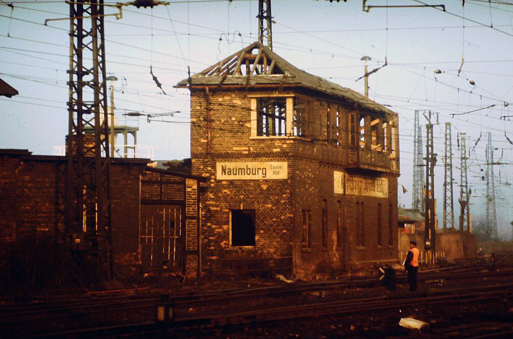 Als 1956 in Naumburg die neuen Gleisbildstellwerke B2/W2 (Richtung Bad Kösen) und W1 (Richtung Leißling) in Betrieb gingen, hatte das alte Stellwerk Nm unmittelbar neben dem Bw ausgedient. In den 1970er Jahren waren in dem Gebäude dann ebenerdig der Dienstraum für die Aufsicht Güterbahnhof, Zugfertigsteller und Zugabfertiger sowie Waschräume untergebracht. Im oberen Stockwerk befanden sich die Aufenthalts- und Umkleideräume für die Rangierer des Güterbahnhofs.
Mit der Errichtung eines Sanitärtracktes mit Umkleideräumen an der sogenannten  Panzerstraße  wurde das Stellwerk geräumt und stand nun leer. Das Personal war nun im sogenannten  Posten 1  untergebracht. Dieses kleine Gebäude stand unmittelbar neben dem alten Stellwerk und bestand aus nur einem Raum, sehr eng ging es hier nun für Rangierer und Aufsicht des Gbf zu. 1991 wurde mit dem Abriß des alten Stellwerks begonnen. Nach dem Abriss des alten Stellwerks war nun Platz vorhanden und man beschloss Posten 1 um einen weiteren Raum zu erweitern. Dazu musste der Posten nun geräumt werden, um Baufreiheit zu schaffen. Aufsicht, Zugfertigsteller und Zugabfertiger zogen in die Güterabfertigung um. Für das Rangierpersonal wurde ein ausgemusterter Bag Wagen nach Gleis 43 direkt an den Prellbock gestellt und an die Dampfvorheizanlage der Reisezüge angeschlossen. Die Station dafür befand sich unweit hinter dem Prellbock. Bahnhofswagen 1, in dem sich verschiedene Gerätschaften befanden (u.a. sogenannte Aufgleisschuhe bei leichtenRangierentgleisungen) kam dann auch wieder nach Gleis 43, so das über einen längeren Zeitraum zwei Bag Wagen dort standen.
Somit diente der zweite Wagen als Aufenthaltsraum für das Rangierpersonal bis zur Fertigstellung von Posten 1. Übrigens hat sich dessen Erweiterung nicht mehr so richtig gelohnt. Mit dem Wegfall der Rangierarbeiten auf dem Güterbahnhof wurde er bald wieder dichtgemacht. (Text & Foto: R. Reimer)
