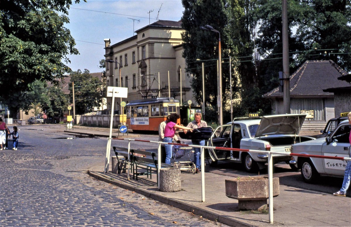 Am 19.08.1990 auf dem Vorplatz in Naumburg Hbf. Ein Tw der Naumburger Straßenbahn, mit Werbung für die Mitteldeutsche Zeitung, wartet auf die Abfahrt Richtung Innenstadt. Und ein Taxifahrer verlädt einen Kinderwagen in seinen Wolga m-24. (Foto: Andreas Rossel)