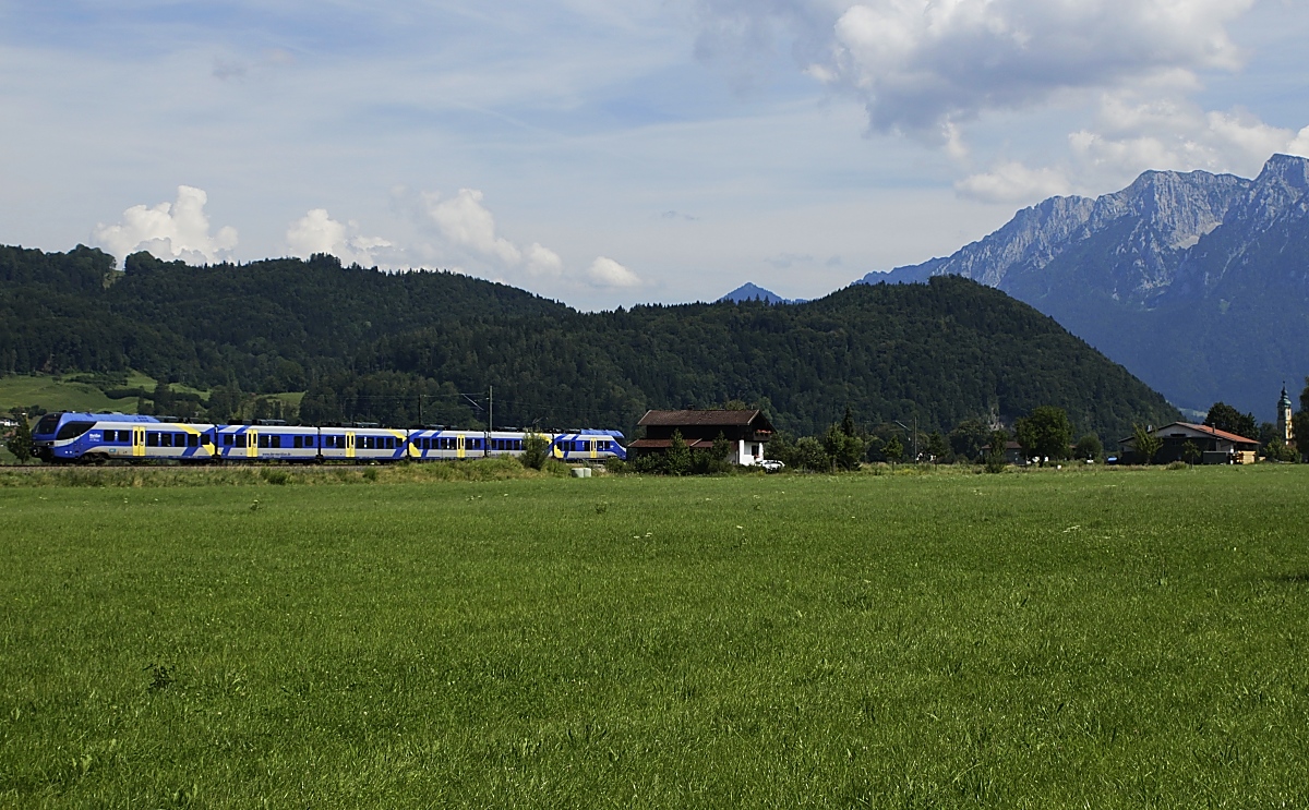 Auf den Strecken von München nach Kufstein und Salzburg setzt die Bayerische Regionalbahn (ex Meridian) sechsteilige Stadler-Flirt 3 ein, ein unbekannter Flirt 3 fährt am 20.07.2020 bei Niederaudorf in Richtung München. Der Hügelzug im Hintergrund liegt bereits auf der anderen Innseite in Österreich, rechts im Hintergrund der Zahme Kaiser.