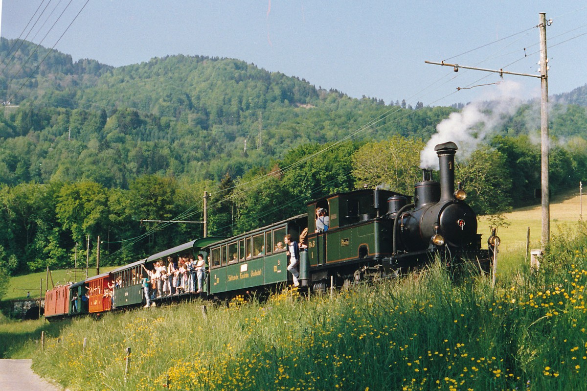 BC: Dampf-Festival auf der Blonay-Chamby-Bahn während dem Pfingstwochenende 1986. Was sich seit dem Jahre 1986 verändert hat: Der Bahnfotograf war damals noch mit der analogen Canon-Spiegelreflexkamera und lichtempfindlichen Kodak 100 ASA Filmen unterwegs. Auch wurde der lange Dampfsonderzug mit 5 Wagen damals noch mit zwei ehemaligen RhB-Lokomotiven geführt. Auf der Fahrt von Blonay nach Chamby leistete die Ge 4/4 181 (1916), ehemals RhB Bernina der G 3/4 1  Rhätia  (1889), ehemals RhB, Schiebedienst. Die Aufnahme entstand im Mai 1986 bei Cornaux. Die Rhätia stand seit dem Jahre 1970 bei der BC im Einsatz. Ab dem Jahre 1988 dampft sie nach einer aufwendigen Aufarbeitung wieder im Bündnerland auf ihren ehemaligen Stammstrecken.
Foto: Walter Ruetsch 