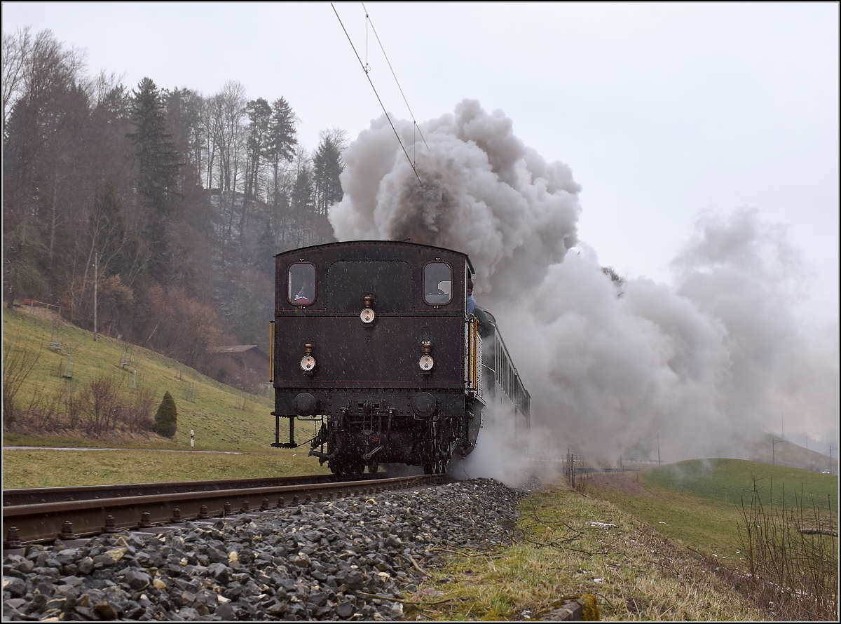 Dampflok Ed 3/4 Nr. 2 der Solothurn-Münster-Bahn bei Dürrenroth. Betreut wird die Lok durch den Verein historische Emmentalbahn. Mit im Gepäck hat sie zwei vierachsige Leichtstahlplattformwagen und einen K2. Vom Feldweg ist eine érstaunliche Position möglich, der ist hier mit einem Mäuerchen aus dem Bahndamm geschnitten. Februar 2018.