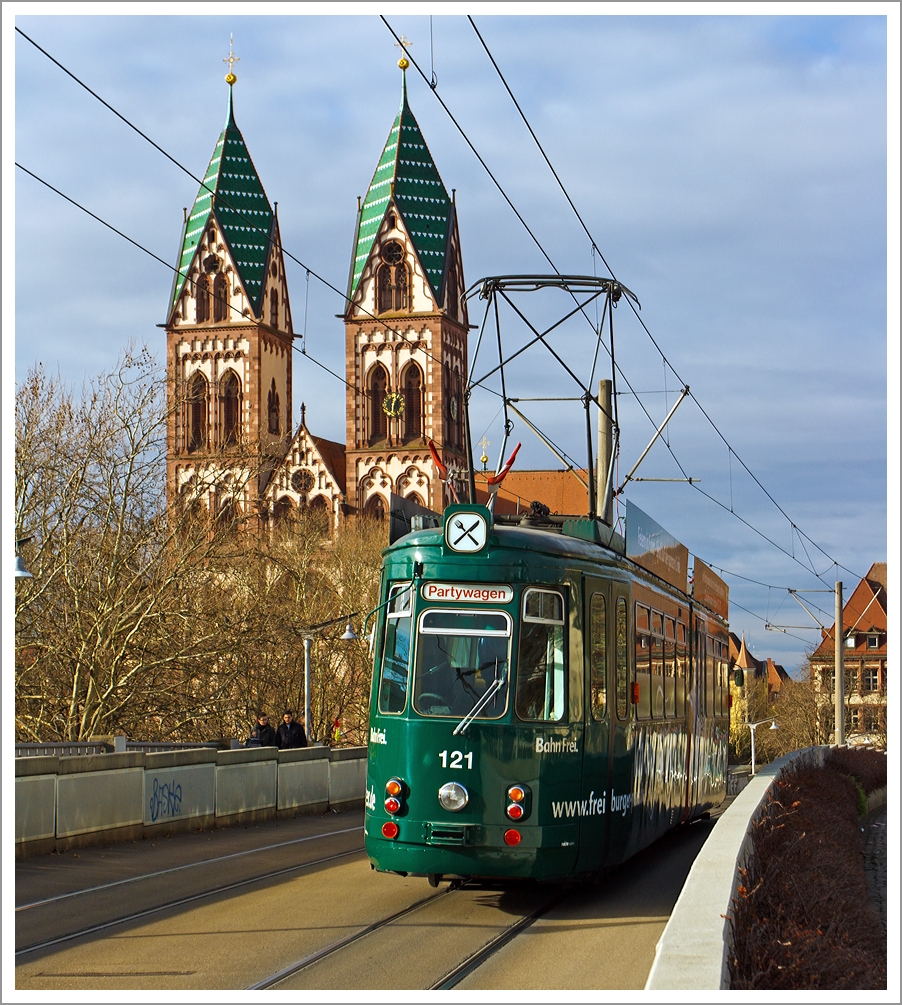 Der Partywagen 121 der Freiburger Verkehrs AG (VAG) überquert die Stühlingerbrücke (Freiburg im Breisgau) am 07.12.2013, im Hintergund die Herz-Jesu-Kirche.

Der Wagen ist ein GT4 (vierachsige Straßenbahn-Kurzgelenktriebwagen in Zweirichtungsausführung) und wurde 1968 von der Waggonfabrik Rastatt gebaut, 1995 erfolgte der Umbau zum Partywagen. 

Technische Daten: 
Achsformel:  (1A)(A1)
Spurweite:  1.000 mm (Meterspur)
Länge über Kupplung:  17.430 mm
Breite:  2.200 mm
Leergewicht:  19.000 kg
Höchstgeschwindigkeit:  50 km/h
Stundenleistung:  2 × 100 kW = 200 kW
Stromsystem:  600 Volt Gleichstrom

Zwischen 1962 und 1968 beschaffte die Freiburger Verkehrs AG 19 dieser GT 4 nach Vorbild von der Stuttgarter Straßenbahnen entwickelten Kurzgelenktriebwagen des Typs SSB GT4 in Zweirichtungsversion, mit einigen Änderungen. Bei der Maschinenfabrik Esslingen wurden 11 Wagen gebaut (1962 und 1966) und 8 weitere wurden 1967 und 1998 aber von der Waggonfabrik Rastatt gebaut, weil die Maschinenfabrik Esslingen keine Straßenbahnen mehr herstellte. 
