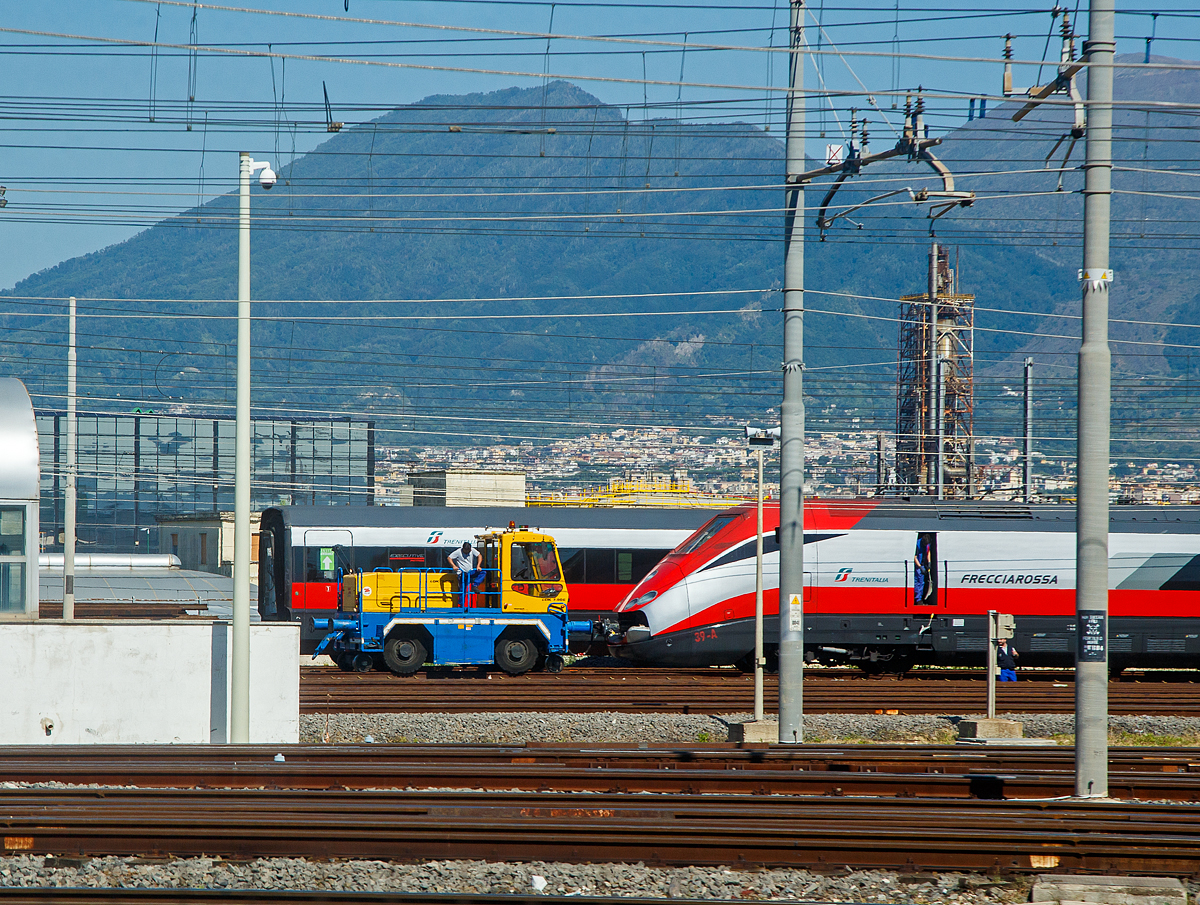 Der Trenitalia am 14.07.2022 aus dem Zug ins Depot in Neapel (Napoli) geschaut: Hier vor dem Trenitalia ETR 500 39 der Zephir Zweiwege-Rangierer (Elektro/Akku Rangierfahrzeug) vom Typ LOK 7.90E. 

Der italienische Hersteller ZEPHIR SpA in Modena ist seit über 50 Jahren der Marktführer in Europa für innovative Zweiwege Rangier Locotraktoren und industrielle Rangiertraktoren. Durch die Gummibereifung (Traktion am Gleis) hat ein solches Fahrzeug einen mehr als 2 x höheren Reibungskoeffizient als bei einer Lok.

TENISCHE DATEN von dem Rangierer:
Spurweite: 1.435 mm (normalspur)
Länge über Kupplung: 4.800 mm
Breite ca.: 2.500 mm
Höhe ca.: 3.400 mm  
Gewicht: 16.000 kg
Motorleistung: 30 kW 
Zugkraft: 70 kN 
Max. Anhängelast: 1.400 t 
Höchstgeschwindigkeit: 7 km/h