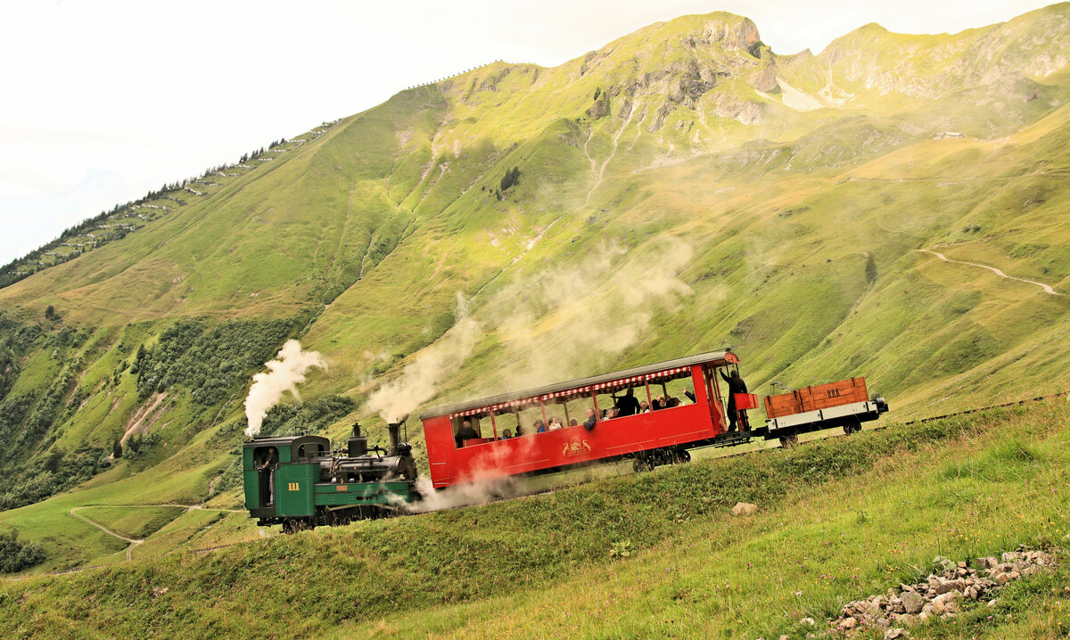 Die einstige Wengernalpbahn-Lok, heute Nr.5, im Abstieg in der Chuemaad. Der Wagen ist der Dreiachser Salon-Wagen Nr.27 mit einer unteren Achse und oben einem Drehgestell. Bei der Lok 5 handelt es sich um die WAB-Lok 1 aus dem Jahre 1891, die 1912 nach deren Elektrifikation zur BRB kam. 3.August 2023 