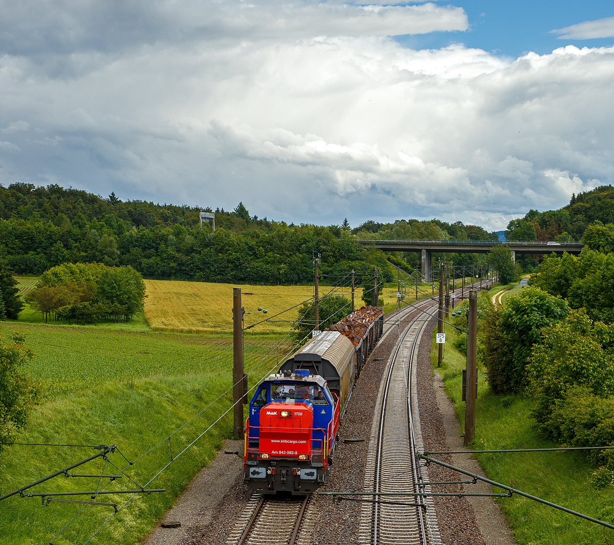 Die SBB Cargo Am 843 092-8 (eine modifizierte Vossloh MaK 1700) fährt am 17.06.2016 mit einem kurzen Güterzug durch Bietingen in Richtung Schaffhausen. 

Einen lieben Gruß an den freundlichen Lokführer zurück.

Die Lok wurde 2005 von Vossloh in Kiel unter der Fabriknummer 1001440 gebaut und an die SBB Cargo AG in Basel geliefert. Sie gehört zu den letzten fünf Loks der Serie an die SBB Cargo, diese fünf Maschinen (Am 843 091 bis 095) sind zusätzlich mit der deutschen Zugsicherung Indusi ausgerüstet worden und haben einen zweiten Führerstand auf der rechten Seite. 

Die SBB Am 843 ist eine moderne Rangier- und Güterzugslokomotive der Schweizerischen Bundesbahnen (SBB). Sie ersetzt ältere Rangierlokomotiven wie die SBB Bm 4/4 und SBB Bm 6/6. Eingesetzt wird die Am 843 von der Division Infrastruktur (843 001ff), der Division Personenverkehr (041ff) und von SBB Cargo (050ff). Die Division Infrastruktur verwendet die Am 843 vor allem in den grossen Rangierbahnhöfen, Personenverkehr in Basel und Chiasso und bei SBB Cargo dient sie vor allem für Zustellfahrten im Nahgüterverkehr.

Die Am 843 verfügt über einen Mikropartikelfilter und gilt als eine der saubersten Diesellokomotiven. Die Filteranlage verhindert, dass 95 % der Russpartikel in die Umwelt abgegeben werden. Die Am 843 basiert auf den dieselhydraulischen Standardlokomotiven des Typs G 1700-2 BB des Kieler Schienenfahrzeugherstellers Vossloh, ist aber im Gegensatz zur Standard-Version auf den in der Schweiz üblichen Linksverkehr ausgelegt.

Anfang der 2000ter musste eine neue Lokomotive angeschafft werden, welche allen Anforderungen gerecht wurde. So musste die Lok über hervorragende Langsam Fahreigenschaften verfügen um im Verschubdienst eingesetzt werden zu können. Die SBB-Cargo wollte aber auch im Nahbereich Zustellfahrten machen, was eine Höchstgeschwindigkeit von 100 km/h erfordernde und gute Leistung. Schließlich fiel die Wahl auf die MaK 1700 BB, welches bei Vossloh in Kiel entstehen sollte. Vossloh entstand aus der ehemaligen und bekannten Unternehmen Maschinenfabrik Kiel (MaK). Dies war die erste größere Serie die der Kieler Lokomotivbau in die Schweiz verkaufen konnte. Noch bei der letzten Ausschreibung haben die Kieler gegen das Konsortium um Alstom verloren. Ebenfalls eine Neuheit war, dass die SBB erstmals eine größere Anzahl dieselhydraulischer Lokomotiven anschafften, nachdem bei der Am 841 noch einer dieselelektrischen Lokomotive der Vorzug gewährt wurde.

Der Lokrahmen besteht aus Walzträgern und massiven Blechen, welche in Schweißkonstruktion miteinander verbunden wurden. Dadurch entsteht ein stabiler und robuster Grundaufbau, welcher der Lok die notwendigen Festigkeiten verleiht. Im Lokrahmen wurde eine so genannte Umweltwanne montiert, welche aus dem Fahrmotor austretenden Flüssigkeiten (Mineralölen und Wasseremulsionen) auffängt, diese können mit Hilfe eines Ablasshahnes entleert und fachmännisch entsorgt werden.

Der vordere längere Vorbau beinhaltet neben dem Dieselmotor auch die notwendige Kühlanlage und das Antriebsgetriebe. Der kürzere hintere Vorbau enthält neben der Druckluftanlage auch die elektrischen Komponenten wie die Batterieladung.

Zwischen den beiden Vorbauten befindet sich das Mittelführerhaus, welches über die zwei diagonal gegenüberliegenden Eingangstüren betreten werden kann. In ihm sind alle für den Lokführer notwendigen Einbauten vorhanden. Ein Führersitz je Fahrpult und Fahrrichtung, welcher mit Arm- und Rückenlehnen ausgerüstet ist, erlaubt die sitzende Bedienung der Lokomotive. Dieser Führersitz ist drehbar gelagert und kann zusammengeklappt und unter den Führertisch verschoben werden. Dadurch ist auch die stehende Bedienung der Lokomotive ohne Behinderung möglich. Zur Entlastung der Füße sind auch verstellbare Fußstützen montiert. Der Fußboden ist mit einem Profilgummibelag belegt worden, der eine einfache Reinigung und dennoch einen guten Stand erlaubt.

Angetrieben wird die Lokomotive von einem 12-Zylinder-4Takt-Dieselmotor vom Typ Caterpillar 3512 B DI-TA-SCAC, dieser erbringt mit Hilfe der beiden Abgasturbolader und der Ladeluftkühlung eine maximale Leistung von 1.500 KW (2.040 PS). Seine höchste Drehzahl beträgt 1.800 U/min. Er wird mit Hilfe eines elektrischen Anlassers gestartet und ist elektronisch geregelt. Dadurch ist es möglich, den Motor bestmöglich im optimalen Leistungsbereich zu betreiben. Sein Gewicht beträgt mit 322 Liter Schmieröl und 134 Liter Kühlwasser 7.700 kg.

Die vom Dieselmotor erzeugte Leistung wird mittels einer Gelenkwelle auf das hydrodynamische Getriebe (Turbowendegetriebe), vom Typ Voith L5r4zseU2, übertragen. Das Getriebe hat eine maximale Leistung von 1.400 kW. Es beschränkt somit die Leistung der Lokomotive und verhindert zugleich, dass der Fahrmotor überlastet werden kann. Seine maximale Drehzahl ist gleich groß, wie jene des Fahrmotors. 

Das Turbowendegetriebe besitzt für jede Fahrrichtung zwei Drehmomentwandler. Dem eigentlichen Wandlergetriebe ist eine mechanische Getriebe nachgeschaltet, das eine niedrige für den Rangierbetrieb bestimmte Schaltung und eine höhere für den Streckenbetrieb bestimmte Schaltung zur Verfügung zu stellen. Diese Umschaltung darf jedoch erst im Stillstand erfolgen.

Die Achsen in den Drehgestellen werden über Gelenkwellen vom Turbowendegetriebe angetrieben. Die Übertragung auf die Achsen erfolgt mit Hilfe von Stirnradgetrieben mit Kegelradvorgelege.

Technische Daten:
Spurweite: 1.435 mm (Normalspur)
Achsformel: B'B'
Länge über Puffer: 15.200 mm
Höhe: 4.220 mm
Breite: 3.080 mm
Drehzapfenabstand: 7.700 mm
Achsstand im Drehgestell: 2.400 mm
Dienstgewicht:  80 t
Höchstgeschwindigkeit: 100 km/h (40 km im Rangiergang)
Installierte Leistung: 1.500 kW (2.040 PS)
Anfahrzugkraft:  249 kN
Treibraddurchmesser:  1.000 mm
Motorentyp:  Caterpillar 3512B DI-TA-SCAC
Nenndrehzahl: 1.800/min
Kleinster bef. Halbmesser:  60 m
Tankinhalt: 3.500 l