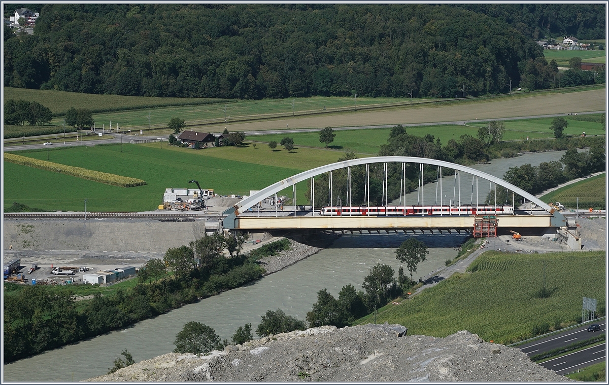 Die Suche nach einem besseren Fotostelle für die neue Rhonebrücke führten mich an Nahe an den sicheren Abgrund. Doch Abschrankungen des Kieswerkes beachtend und so auf öffentlichem Grund bleibend, hat man einen ungefährlichen und schönen Blick auf die neuen Rhonebrücke, die demnächst an ihren definitiven Standort verschoben werden wird. Auf dem Bild befährt ein  Walliser Domino  die Brücke, welcher für die seit Fahrplanwechsel teilweise fehlenden Halte der IR als RE zwischen St-Maurice und Aigle verkehrt. 26. August 2016 