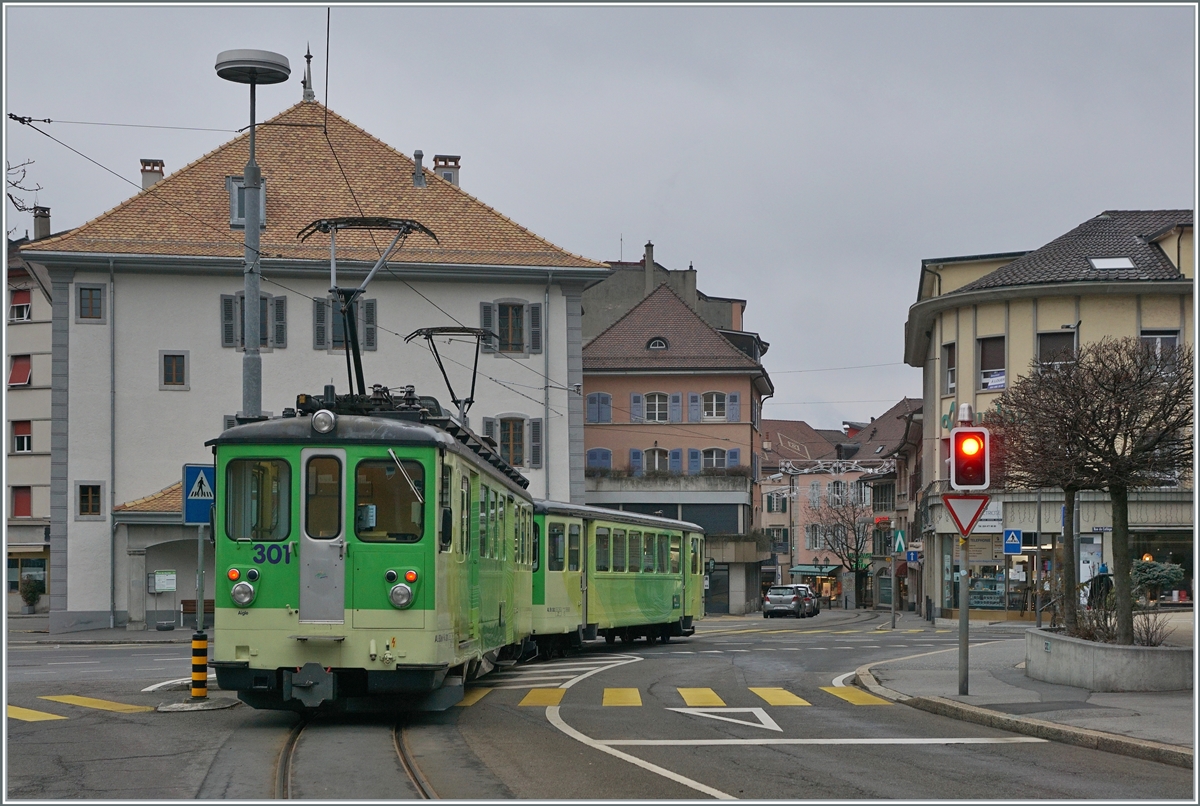 Ein A-L Regionalzug von Leysin hat Haltstelle Aigle-Place-du-Marché hinter sich gelassen und fährt nun auf der Strasse durch die Altstadt von Aigle zum Bahnhof Aigle. 

3. Jan. 2021