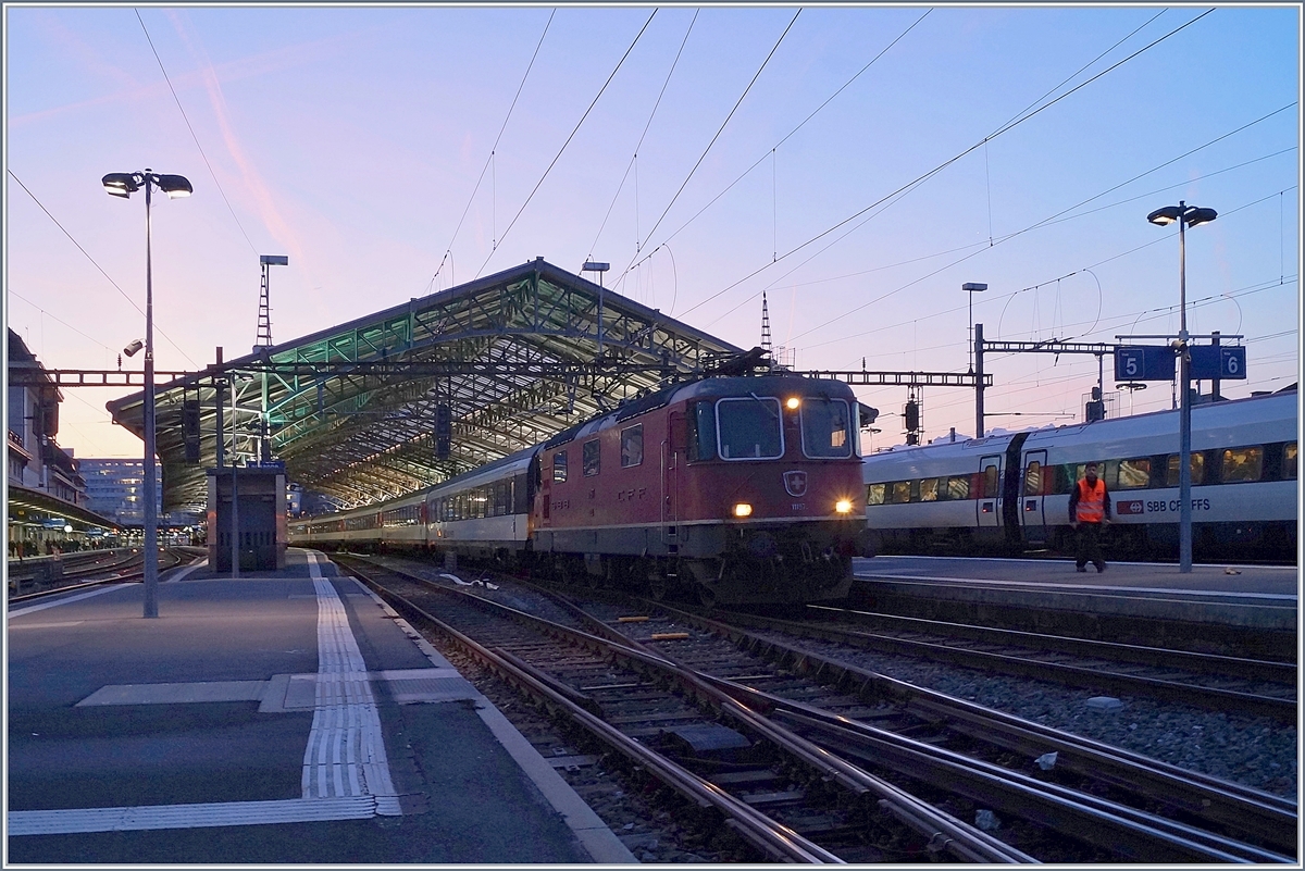 Ein leichtes Morgenrot breitet sich über dem noch im Schatten liegenden Bahnhof von Lauanne aus, im Vordergrund ist eine SBB Re 4/4 II mit ihrem RE aus St-Maurice eingetroffen. 

20. Feb. 2019