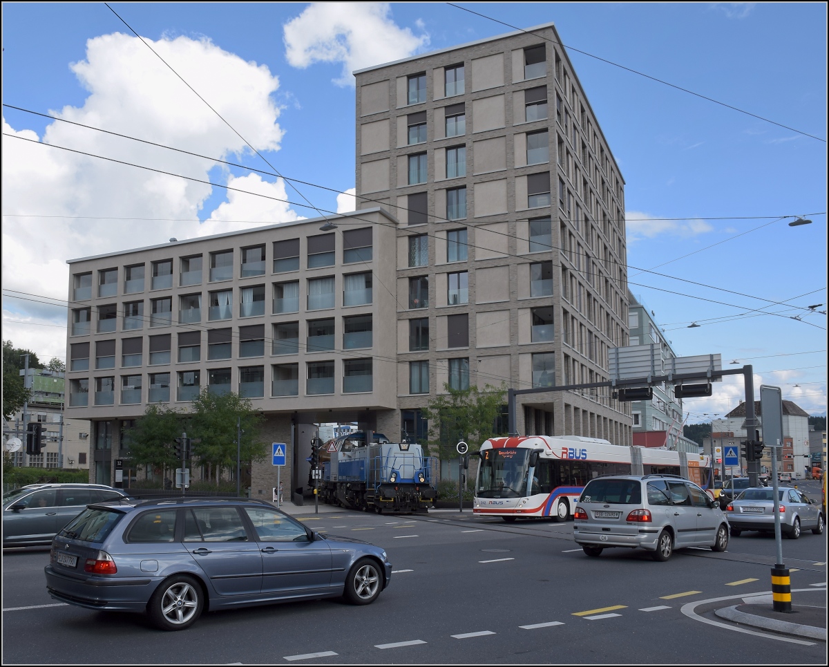 Gravita Am 847 003 'Littau' wartet mit einen schweren Stahlzug von der Emmenwaid unter dem Eckhaus. Strassenverkehr hat der Bahnfotograf gewöhnlich nicht gern im Bild. Hier aber passt alles zusammen. August 2021. 