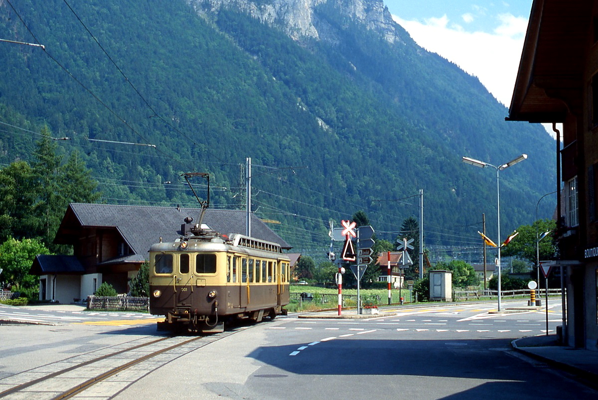 Kurz nach Verlassen des Bahnhofs Innertkirchen überquert der ABDeh 4/4 301 der Berner Oberland-Bahn im Juni 1990 die Kreuzung von Grimsel-, Susten- und Dorfstraße