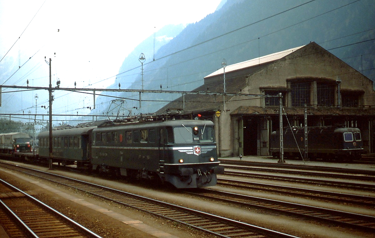 Mit einem Autoshuttle durchfährt Ae 6/6 11403 im Juli 1983 den Bahnhof Erstfeld. Leider waren zu diesem Zeitpunkt bei vielen Ae 6/6 die Alu-Zierstreifen schon entfernt.