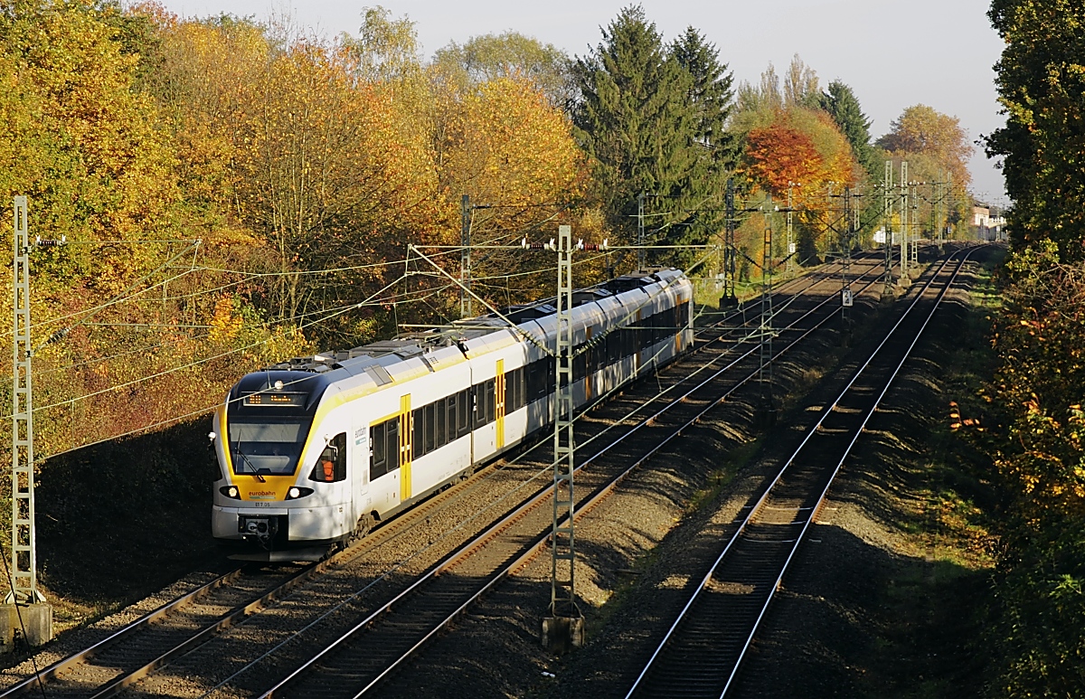 Mit den Eurobahn-Stadler FLIRT und dem RE 13 (Hamm (Westfalen) - Venlo/Niederlande) unterwegs: Auf dem 2,5 km langen Teilstück Erkrath - Hochdahl der 1841 eröffneten Düsseldorf-Elberfelder Eisenbahn muss ein Höhenunterschied von 82 m überwunden werden. Zunächst wurden die Züge mittels Seil von einer stationären Dampfmaschine am Ende der Steigung in Hochdahl hinaufgezogen, später wurde die Seilwinde durch eine Umlenkrolle ersetzt und talwärts fahrende Züge bzw. eigens dafür in Hochdahl stationierte Lokomotiven zogen die bergwärts fahrenden hinauf. Dieses Verfahren wurde erst 1926 aufgegeben, als ausreichend zugkräftige Lokomotiven zur Verfügung standen. Am 01.11.2015 fährt ET 7.05 die Steilrampe hinunter, der Beginn der Gefällestrecke ist im Hintergrund erkennbar.