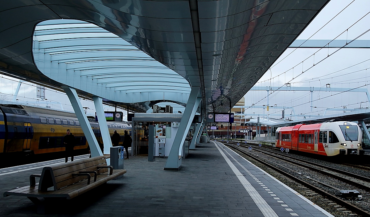 Nicht nur das Empfangsgebäude, sondern auch die Bahnsteige in Arnhem Centraal sind archítektonisch beeindruckend (02.01.2018). Die Bahnsteigdächer sind teilweise verglast, um das Tageslicht durchzulassen. Auf jedem Bahnsteig gibt es ausreichend Sitzgelegenheiten, einen Kiosk und einen geschlossenen Warteraum. Ein solcher Service ist leider nicht überall selbstverständlich. Im Hintergrund wartet ein Stadler-GTW 2/6 von Arriva auf die Abfahrt nach Tiel.