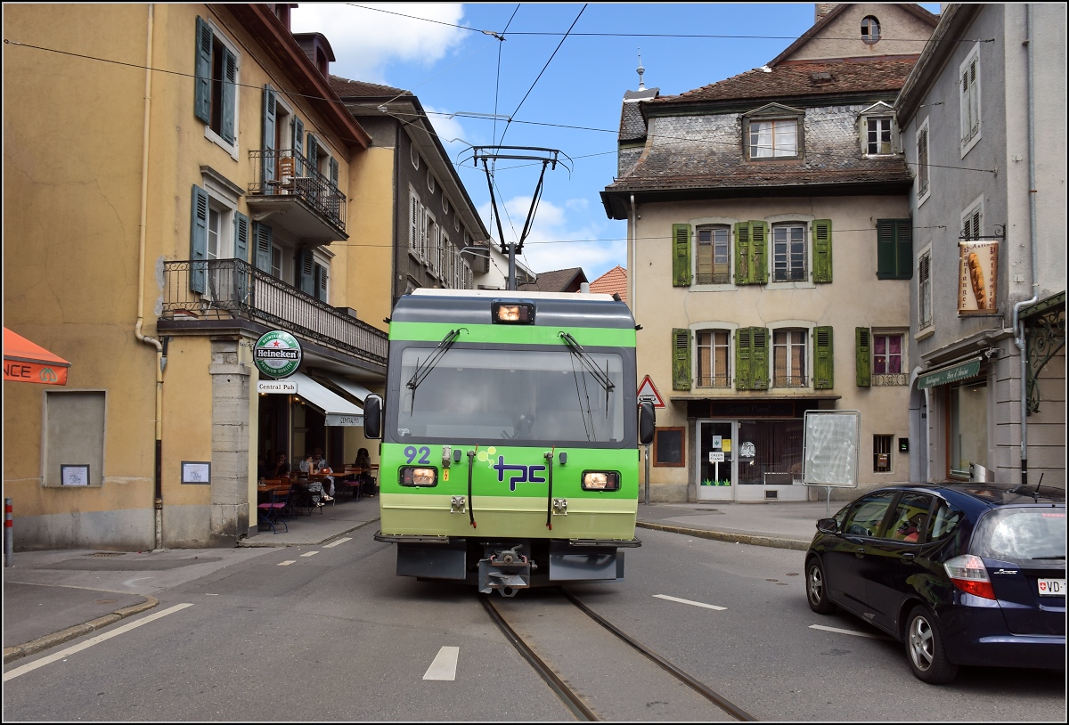 Ortsdurchfahrt in Bex. Das Auto ist in Sicherheit gebracht, es kommt TPC-Triebwagen 92 der Bex–Villars-sur-Ollon–Bretaye-Bahn entgegen. Juli 2017. 