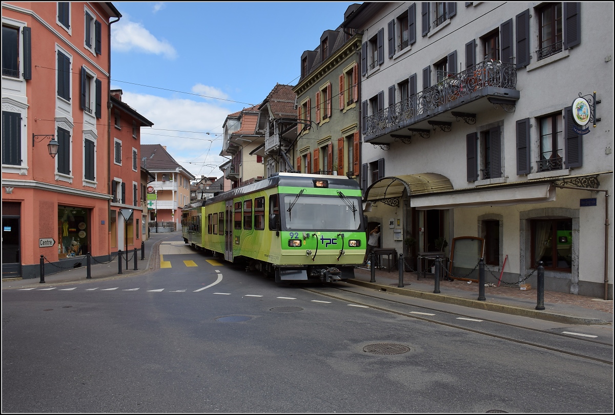 Ortsdurchfahrt in Bex. Linksabbieger im Gegenverkehr, der TPC-Triebwagen 92 nutzt die falsche Straßenseite. Juli 2017.