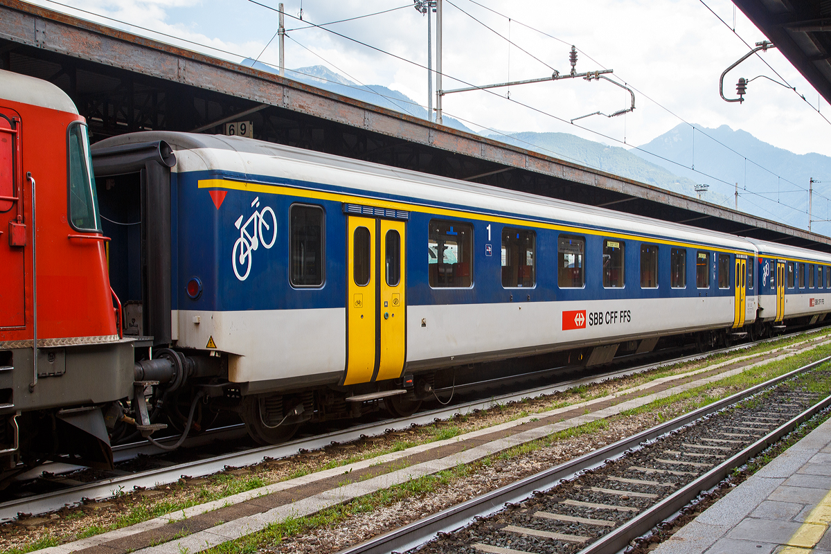 
SBB – 1.Klasse Personenwagen A 50 85 18-35 029-5, ein modernisierte Einheitswagen I (EW1), eingereiht in einem Pendelzug am 05.08.2019 im Bahnhof Domodossola.

Die Einheitswagen I sind die Nachfolger der Leichtstahlwagen und wurden zwischen 1956 und 1967 gebaut. Sie waren ursprünglich in SBB-Grün lackiert und hatten ein Gewicht von 28 bis 32 Tonnen, eine Länge von 23,7 m und eine zulässige Höchstgeschwindigkeit von 140 km/h.

Damit die Einstiege über den Drehgestellen angeordnet werden konnten, mussten die Drehgestellrahmen in der Mitte gekröpft ausgeführt werden. 

Die Senkfenster sind einteilig, einfach verglast und rahmenlos; die Scheiben werden beim Öffnen bis zur Hälfte in die Wagenseitenwand versenkt.

Über 360 Einheitswagen I wurden ab 1984 für die Neuen Pendelzüge (NPZ) umgebaut. Sie bekamen eine Lackierung nach dem NPZ-Schema (weiss-blau mit gelben Türen), entsprechende Sitzpolsterung und eine neue Inneneinrichtung. Automatische Türen (außenbündig) für den kondukteurlosen Betrieb wurden in einem zweiten Schritt ab 1992 eingebaut. Diese Wagen werden im Regionalverkehr sowohl als NPZ wie auch mit t Re 4/4 II eingesetzt. Dazu wurden auch alle Steuerwagen mit Personenabteilen der Einheitstypen I und II entsprechend umgebaut. 

Während per 2018 die Einheitswagen II fast vollständig ausrangiert sind, sind im Gegensatz noch viele Einheitswagen I im Dienst.

TECHNISCHE DATEN:
Spurweite: 1.435 mm (Normalspur)
Länge über Puffer: 23.700 mm
Drehzapfenabstand: 17.600 mm
Achsabstand im Drehgestell: 2.700 mm
Eigengewicht: 32 t
Sitzplätze: 60 in der 1.Klasse und Fahrradabteil
Bremse: O-R 43t (P43t) K