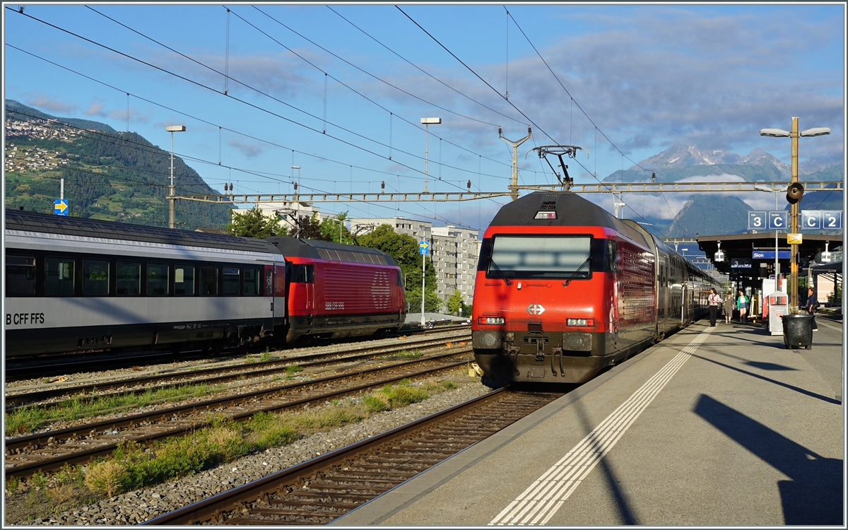 SBB Re 460 in Sion: Links wartet eine SBB Re 460 mit ihrem HVZ IR90 auf ihren Einsatz am Montag, während die Re 460 rechts im Bild ihren IR 90 nach Genève Aéroport schiebt. 

25. Juni 2022