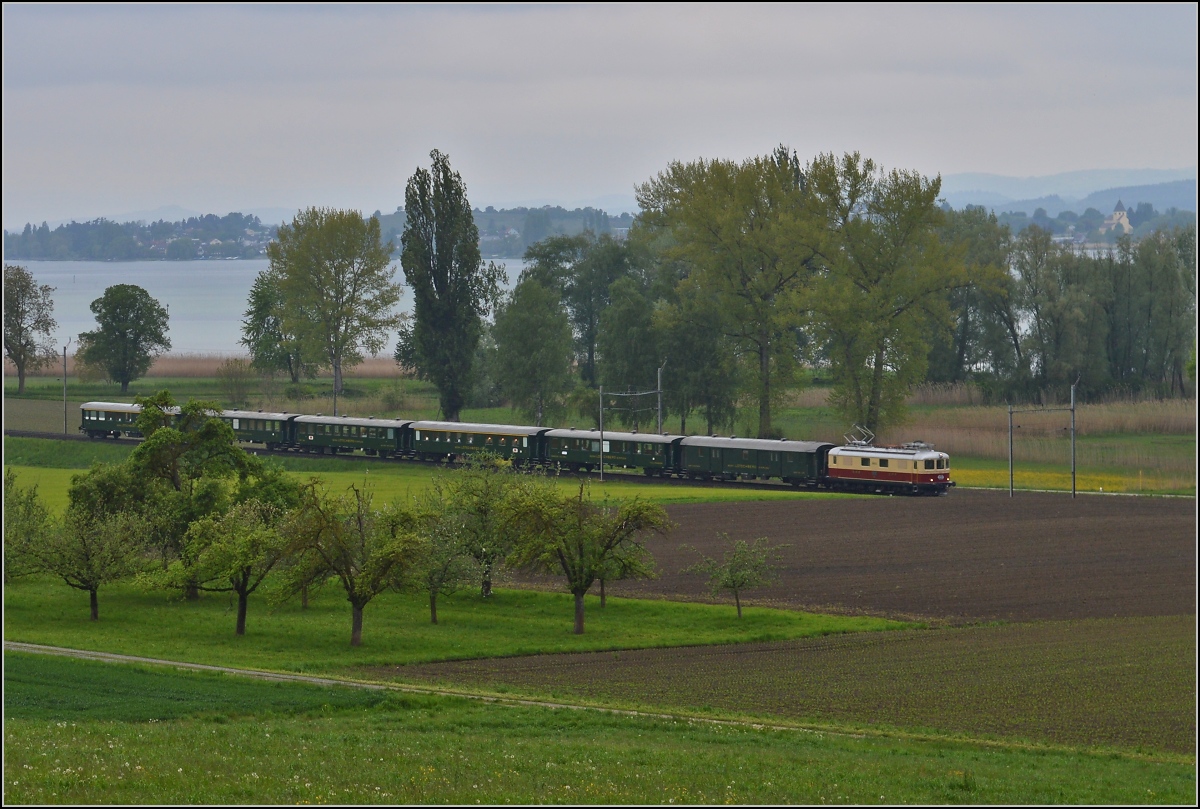 TEE am See. Die Re 4/4 I 10034 im Rot/Creme-Gewand und historischen SBB-Wagen am Untersee bei Triboltingen. Rechts im Hintergrund St. Georg auf der Reichenau, Teil des Unseco Weltkulturerbes. Mai 2014.