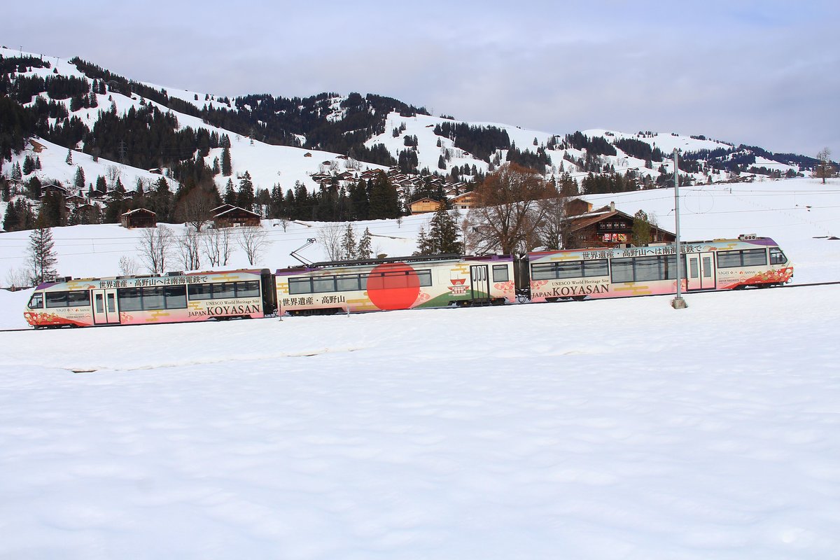 Triebzug 5002 der MOB zwischen Schönried und Gruben, 4.Februar 2021. Auf dem Zug steht 世界遺産・高野山へは南海電鉄で . Das heisst:  Zum Weltkulturerbe Kôya-san mit der elektrischen Nankai-Eisenbahn! . Die Nankai Privatbahn (1067 mm-Spur) betreibt ein Netz von 154, 8 km (davon zwei ca. 60 km lange Hauptstrecken) von der Stadt Ôsaka aus nach Süden. Der Begriff  Nankai  (= Süd-See ) steht für die uralte Nankai-dô Strasse, d.h. die Strasse vom alten Kulturzentrum Kyôto aus nach Süden, Richtung offener Pazifik. Kôya-san ist eine riesige Tempelanlage auf etwa 815 m Höhe tief im dichten Wald; entsprechend romantisch ist die extrem steile Bahnstrecke dorthin. Die Tempelanlage wurde im frühen 9. Jahrhundert gegründet und bildet mit seinen über 100 – im Laufe der Jahrhunderte entstandenen - Gebäuden eine der Urzellen des Buddhismus in Japan. 　