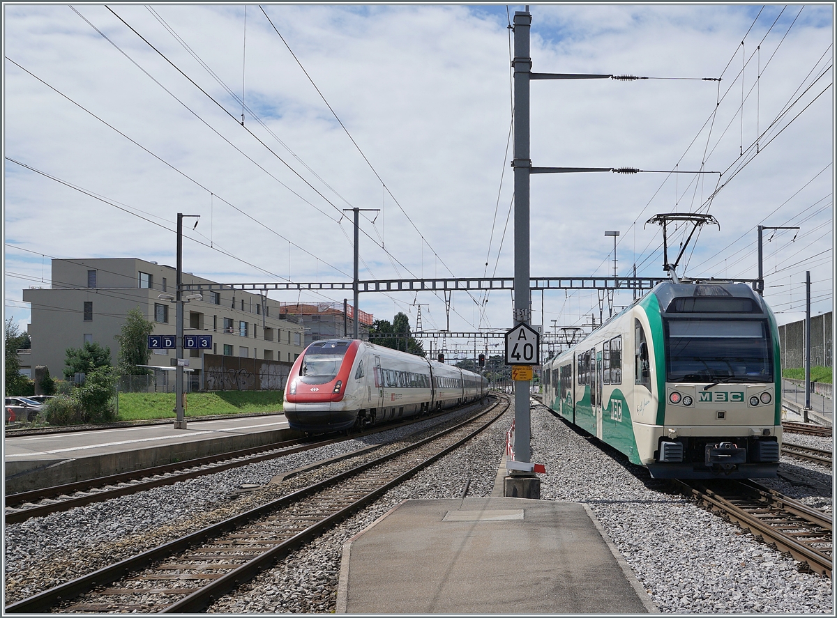 Während der SBB ICN RABe 500 017  Willi Ritschard  auf dem Weg von Genève-Aéroport nach Zürich Moregs erreicht, verlässt ein BAM Regionalzug nach Bière den Bahnhof.

2. August 2021