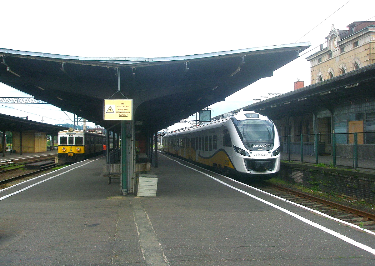 Zwei Generationen von elektrischen Triebwagen treffen am 22.06.2014 in Jelenia Gora/Hirschberg aufeinander, rechts der Flirt 3 140 302-2, links ein EN 57. Von diesen Triebwagen wurden zwischen 1962 und 1994 1.418 Fahrzeuge in Dienst gestellt, sie sind heute noch - teilweise modernisiert - allgegenwärtig. Die gelb-schwarz-weisse Lackierung der Kolej na Dolnym Slasku steht beiden Fahrzeugen gut.