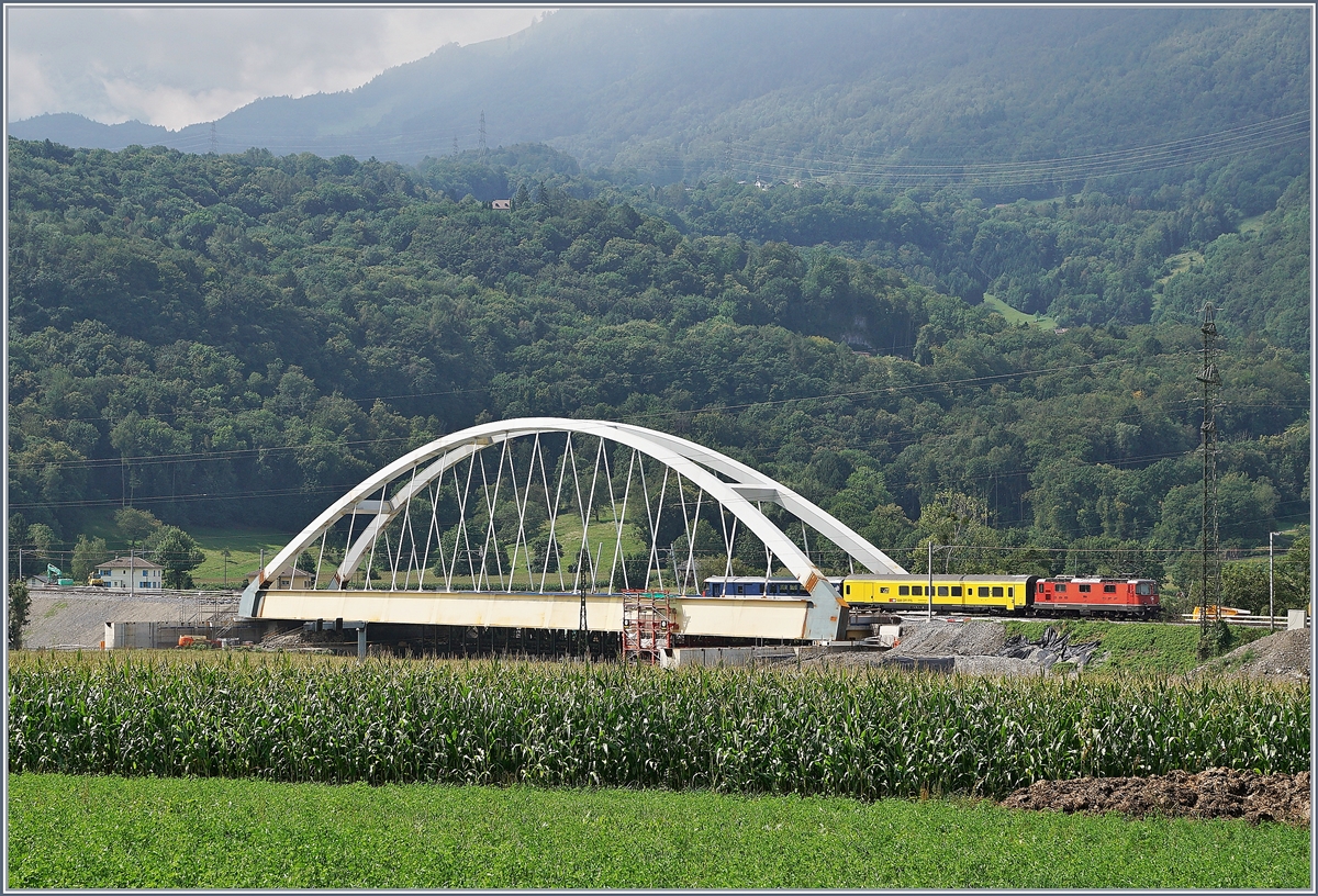 Zwischen Bex und St-Maurice überquert die Strecke Lausanne Birg die Rhone. Die alte Gittereisenbrücke wird nun durch eine sehr gefällige und unübersehbare Neukonstruktion ersetzt. Zu Zeit ist die alte Brücke schon nicht mir in Betrieb und der Verkehr verläuft einspurig über die neue Brücke, wobei vor und nach der Brücke das nördliche Gleis, dann auf der Brücke das Südliche Gleis benutzt wird, so dass die Brücke noch verschoben werden muss. Leider ist es nicht einfach, einen einigermasen guten Fotostandpunkt zu finden. Das Bild zeigt eine SBB Re 4/4 II mit einem Messzug auf der Fahrt Richtung St-Maurice.
19. August 2016