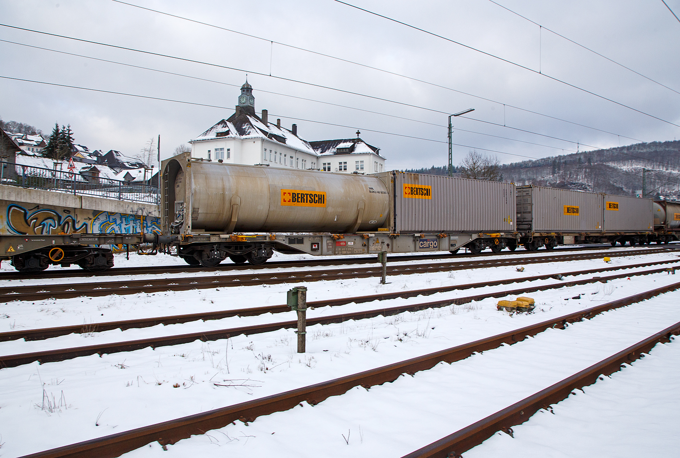 4-achsiger Drehgestell-Containertragwagen 31 85 455 218-3 CH-SBBC, der Gattung Sgnss (60ft), der SBB Cargo AG, im Zugverband am 21.01.2023 bei der Zugdurchfahrt in Niederschelden (Sieg), beladen mit einem 30´ Tank-Containern und einem 30´ ISO-Containern von dem Logistikdienstleister Bertschi AG (Dürrenäsch/Schweiz).

TECHNISCHE DATEN:
Spurweite: 1.435 mm
Anzahl der Achsen: 4 in zwei Drehgestellen
Länge über Puffer: 19.990 mm
Drehzapfenabstand: 14.420 mm
Achsabstand im Drehgestell: 1.800mm
Laufraddurchmesser: 920 mm (neu)
Ladelänge : 18.720 mm  (60 ft)
Höhe der Ladeebene über SOK: 1.155 mm
Höchstgeschwindigkeit: 100 km/h Lastgrenze S / 120 km/h bei Lastgrenze SS und leer)
Max. Zuladung bei Lastgrenze S: 70,0 t (ab Streckenklasse D)
Max. Zuladung bei Lastgrenze SS: 60,0 t (ab Streckenklasse C)
Eigengewicht: 20.000 kg
Kleinster bef. Gleisbogenradius: R 75 m
Bauart der Bremse: DK-GP-A (K)
Bremssohle: Cosid 810
Intern. Verwendungsfähigkeit: RIV
Wageneinrichtungen: 36 Umklappbare Aufsetzzapfen
