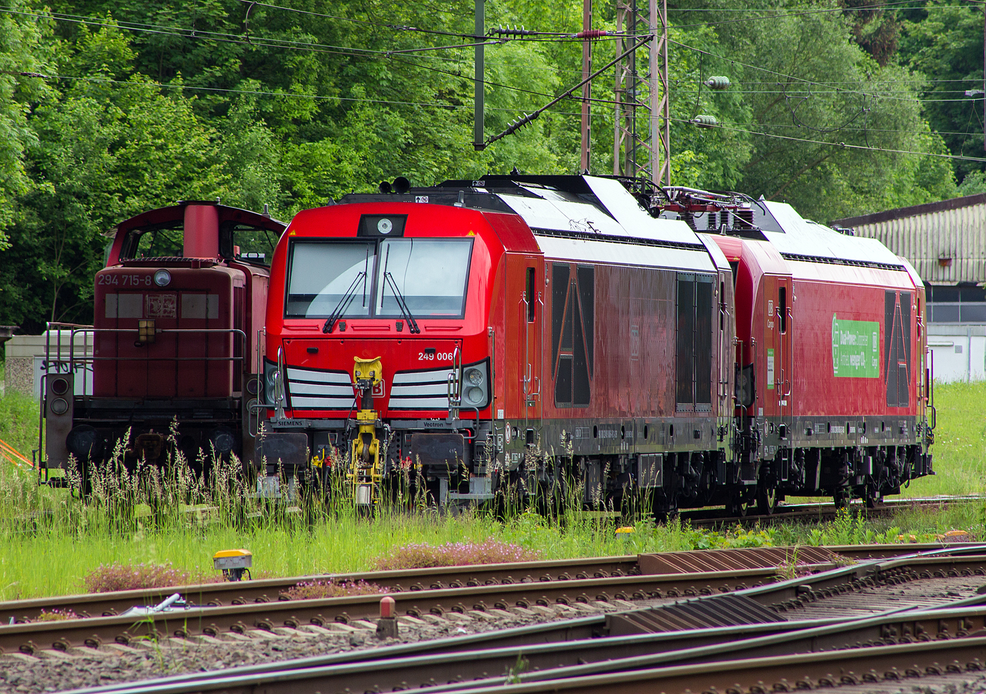Abgestellt unter der Langenauer Brücke in Kreuztal (nahe dem Rbf) sind am 21 Mai 2024, von links nach rechts die Loks der DB Cargo AG:
Die remotorisierte V90 – 294 715-8, ex 294 215-9, ex 290 215-3. Die V90 wurde 1971 von MaK in Kiel unter der Fabriknummer 1000523 gebaut und als 290 215-3an die DB geliefert. Die Ausrüstung mit Funkfernsteuerung und die Umbezeichnung in DB 294 215-9 erfolgte 1996. Die Remotorisierung mit einem MTU-Motor 8V 4000 R41, Einbau einer neuen Lüfteranlage, einem neuem Luftpresser und Ausrüstung mit dem Umlaufgeländer erfolgten 2003 bei der DB Fahrzeuginstandhaltung GmbH im Werk Cottbus. Daraufhin erfolgte die Umzeichnung in die heutige 294 715-8.

Daneben die beiden neuen Zweikraftlokomotiven „Siemens Vectron Dual Mode light“ (BR 249), vorne die 249 006-8 (90 80 2249 006-8 D-DB) und dahinter die 249 003-5 (90 80 2249 003-5 D-DB). Beide Vectron DM light wurden 2022 von Siemens Mobility GmbH in München-Allach unter den Fabriknummern 23061 bzw. 23064 gebaut und waren erst durch Siemens Mobility GmbH als 90 80 2249 003-5 D-SDEHC bzw. 90 80 2249 006-8  D-SDEHC registriert/eingestellt. Erst nach der Abnahme durch die DB Cargo und den Verkauf an diese im März 2024 wurde sie durch die DB Cargo eingestellt. Die Loks der Baureihe 249 haben die Zulassung für Deutschland und eine Höchstgeschwindigkeit von 120 km/h.