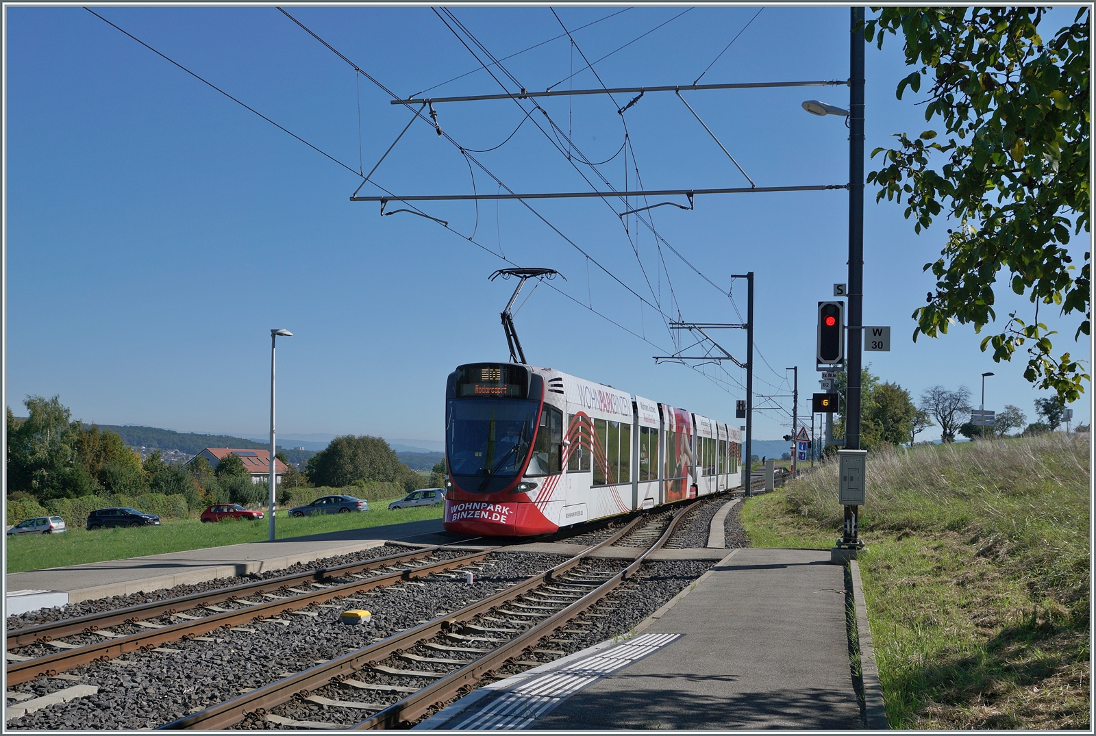 Aus der Grossstadt aufs Land - mit der BLT: Von Basel bzw. wohl Dornach kommend erreicht ein BLT Zug der Linie 10 das im Elsass gelegene Leymen und wird nach der Kreuzung mit dem Gegenzug nach Rodersdorf im Kanton Solothurn weiterfahren, oder anders ausgedrückt - eine Ban drei Kantone, zwei Länder...

Noch ein kleines Detail zum Signal rechts im Bild: Ein kleines  G  macht darauf aufmerksam, dass die Strecke durch den  G egenzug belegt ist.

26. Sept. 2023