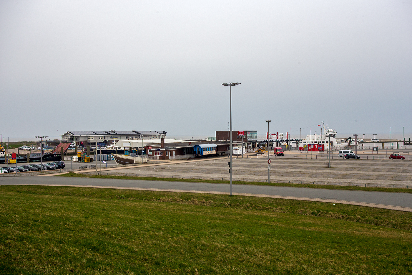 Blick am 11 März 2024 auf den ehemaligen Bahnhof Harle im Außenhafen Harlesiel, heute Fährterminal der SIW - Schifffahrt und Inselbahn Wangerooge (Teil der DB Fernverkehr AG). Hier war bis 1989 die Endstation der 20,1 km langen normalspurigen Bahnstrecke Jever–Harle, auch bekannt als „Tidebahn“ (ex KBS 10007). 

Übrigens ein Teil der KBS 10007 gibt es noch heute, dies ist die schmalspurige Wangerooger Inselbahn. Aber vor dem ehem. Bahnhof liegt auch noch ein Gleisstück der normalspurigen Bahnstrecke, mit einer 3. Schiene zur Aufnahme der beiden Wagen der Wangerooger Inselbahn. 

Die Bahnstrecke Jever–Harle war eine 20,1 Kilometer lange Nebenbahn im Nordwesten von Niedersachsen, die überwiegend dem Verkehr von und zu den Fährschiffen zur Insel Wangerooge diente. Im Januar 1990 wurde die Strecke stillgelegt und abgebaut. Da der Schiffsverkehr nach Wangerooge abhängig von den Gezeiten (der Tide) ist, hatten viele Zugpaare einen täglich wechselnden Fahrplan, weshalb diese Fahrten als Tidezug und die Strecke als Tidebahn bezeichnet wurden.

Die Strecke zweigte am Nordwest-Ende des Bahnhofes von Jever von der Ostfriesischen Küstenbahn ab und verlief weitgehend gradlinig und direkt neben der Landstraße nach Norden. Der wichtigste Zwischenbahnhof stand in Carolinensiel. Von dort führte sie bis in das Vordeichsgelände am Hafen Harle.

Der Bau der Bahn war vom Großherzogtum Oldenburg initiiert worden, um den Badebetrieb auf der einzigen oldenburgischen Nordseeinsel Wangerooge zu fördern. Gebaut wurde sie von der „Jever-Carolinensieler Eisenbahngesellschaft“, einer Aktiengesellschaft unter Führung des Bankhauses Erlanger & Söhne in Frankfurt am Main. Am 1. September 1888 wurde der Abschnitt Jever–Carolinensiel eröffnet; die Bahn endete jedoch nicht im damals preußischen Carolinensiel, sondern an der Friedrichsschleuse auf Oldenburger Gebiet. Der Anschluss zum Anleger Harle erfolgte am 1. Juli 1890. Der Betrieb wurde von Anfang an von den Großherzoglich Oldenburgischen Staatseisenbahnen (GOE) übernommen. Diese kaufte 1897 auch die verlustbringende Strecke. Gleichzeitig übernahm sie ein Seebäderschiff und errichtete die Inselbahn Wangerooge. 1956/1957 wurde der Hafen weiter in das Vordeichgelände verlegt und die Bahnstrecke verlängert.

Auf der Strecke überlagerte sich der nach festem Fahrplan verkehrende Zugverkehr Jever–Carolinensiel und der der Tidezüge Sande–Harle. 1944 verkehrten werktags sechs Zugpaare und ein Tidezugpaar, 1961 drei Zugpaare und ein bis zwei Tidezüge.

Der Betrieb war stets unrentabel. Im Jahr 1966 wurde der Verkehr im Winter eingestellt. Die Bedienung der Zwischenhalte endete 1968. Ab 1981 verkehrten Züge nur noch an verkehrsreichen Tagen, wobei sich der Fahrplan nach der Fähre richtete, der von Gezeiten abhing. Im Jahr 1987 musste das Umsetzgleis in Harle dem Parkplatzausbau weichen, so dass nur noch Schienenbusse verkehren konnten. Ein notwendiger Brückenneubau über das Tettenser Tief war Anlass, die Strecke stillzulegen. Zum Winterfahrplan 1987/1988 kündigte die Deutsche Bundesbahn die Einstellung des Personenverkehrs an. Am 27. September 1987 wurde der Reiseverkehr und am 25. September 1988 der Restverkehr eingestellt. Im Januar 1990 wurde die Strecke stillgelegt und abgebaut. Seitdem dienen große Teile der Trasse als Rad- bzw. Fußweg.

Das Bahnhofsgebäude und ein weiteres Bahngebäude in Carolinensiel werden privat genutzt, das Bahnhofsgebäude steht zudem heute unter Denkmalschutz. Das Bahnhofsgebäude in Harle dient als Verkaufsstelle für Fährtickets zur Insel Wangerooge. Vorhanden sind noch die ehemaligen Bahnhofsgebäude, heute privat genutzt, in Tettens und Garms.
