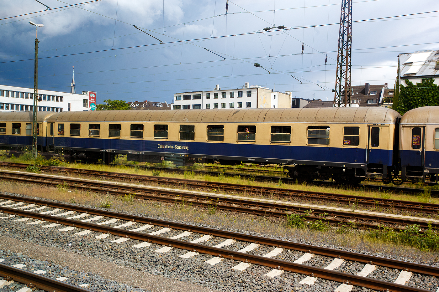 Der erste Klasse Reisezugwagen (Abteilwagen) D-CBB 56 80 10-40 130-1 der Gattung Am 208 der Centralbahn GmbH (Mönchengladbach), eingereiht im Zugverband eines mit 12 Wagen sehr langen Sonder- oder Partyzug der CBB, am 16 Mai 2024 in Köln-West, aufgenommen aus einen Zug heraus.

Der UIC-X-Wagen wurde 1959 von der Waggonfabrik Wegmann & Co. in Kassel gebaut und als DB 11 967 der Gattung A4ümg-54 an die Deutschen Bundesbahn (DB) geliefert. 1966 erfolgte der Umbau und Umzeichnung in D-DB 51 80 10-40 155-3 der Gattung Am 202, im Jahr 1986 wurde er bei Wegmann zum D-DB 51 80 03-40 130-5 Am 036 umgebaut. Im Jahr 2007 ging er als D-CBB 51 80 03-40 130-5 Am 208 an die Centralbahn.

Die Wagen der Gattung Am 208 bieten 60 bequeme Sitzplätze in zehn 6er-Abteilen der 1. Wagenklasse, zudem besitzen sie 2 WC/ Waschräume. Dieser Wagen ist für 140 km/h zugelassen und mehrspannungsfähig.

Schnellzugwagen A4ümg-54 DB
Das Bundesbahn-Zentral-Amt (BZA) Minden der Deutschen Bundesbahn (DB) entwickelte um 1952 ein Typenprogramm für 26,4 m-Fernreisezugwagen (Gruppe-53). Unter der Leitung von Dr.-Ing. Adolf Mielich entstand ein als Baukastensystem ausgelegtes Wagen-Programm. Er griff seine Entwürfe aus der Reichsbahnzeit wieder auf, zudem viele moderne Elemente wie die geschlossenen Gummiwulstübergänge und 1.000 bzw. 1.200 mm breite Übersetzfenster. Von den Vorkriegswagentypen unterschied es sich durch gerade Abteilanzahlen und symmetrische Wagenhälften, welche es ermöglichten, gleiche oder unterschiedliche Wagenklassen sowie Speise- und Packräume miteinander zu kombinieren. Nach neun Probewagen im Jahr 1952 begann 1955 die Serienfertigung. Die B4ümg-54 Reisezugwagen (1.225 Stück) boten den Reisenden der 2. Klasse erstmals nur drei Sitze pro Bank, statt bisher vier. Diese Komfortverbesserung bei dem „Reisezugwagen fürs Volk“ kam bei den Fahrgästen sehr gut an. Die erstklassige Wagenbauart A4ümg-54 (199 Stück) unterstrich beispielhaft den gestiegenen Reisekomfort jener Zeit. In eleganter, dunkelblauer Lackierung verließen die Wagen die Werke und wurden vorrangig in die F-Zugverbände der DB eingereiht. Vervollständigt wurde die Wagengruppe-53 durch die gemischt-klassigen AB4ümg-55 (357 Stück) und ab dem Ende der 1950er-Jahre durch die Halbgepäckwagen der Bauart BPw4üm-58/59 (138 Stück). Durch ihre wegweisenden Neuerungen waren die Wagen, und die aus Ihnen abgeleiteten späteren Umbauten, für die kommenden Jahrzehnte nicht aus den Reisezügen der DB wegzudenken. So verwundert es nicht, dass die letzten Wagen teilweise erst zu Beginn in den 1990er-Jahre ausgemustert wurden, oder dann ein zweites Leben im Museumsverkehr begannen.

TECHNISCHE DATEN:
Spurweite: 1.435 mm (Normalspur)
Länge über Puffer: 26.400 mm
Wagenkastenlänge: 26.100 mm
Wagenkastenbreite: 2.850  mm
Höhe über Schienenoberkante: 4.050 mm
Drehzapfenabstand: 19.000 mm
Achsstand im Drehgestell: 2.500 mm
Drehgestellbauart: Minden-Deutz 330
Leergewicht: 37 t
Höchstgeschwindigkeit: 140 km/h
Sitzplätze in der 1. Klasse: 60
Abteile: 10
Toiletten/Waschraum: 2 
Bremsbauart: KE-GPR
Energieversorgung: Achsgenerator

Die Centralbahn GmbH (Mönchengladbach) gehört zur Centralbahn AG mit Sitz in Basel. Hauptgeschäft ist die Durchführung von Sonderzugfahrten mit eigenen Fahrzeugen.