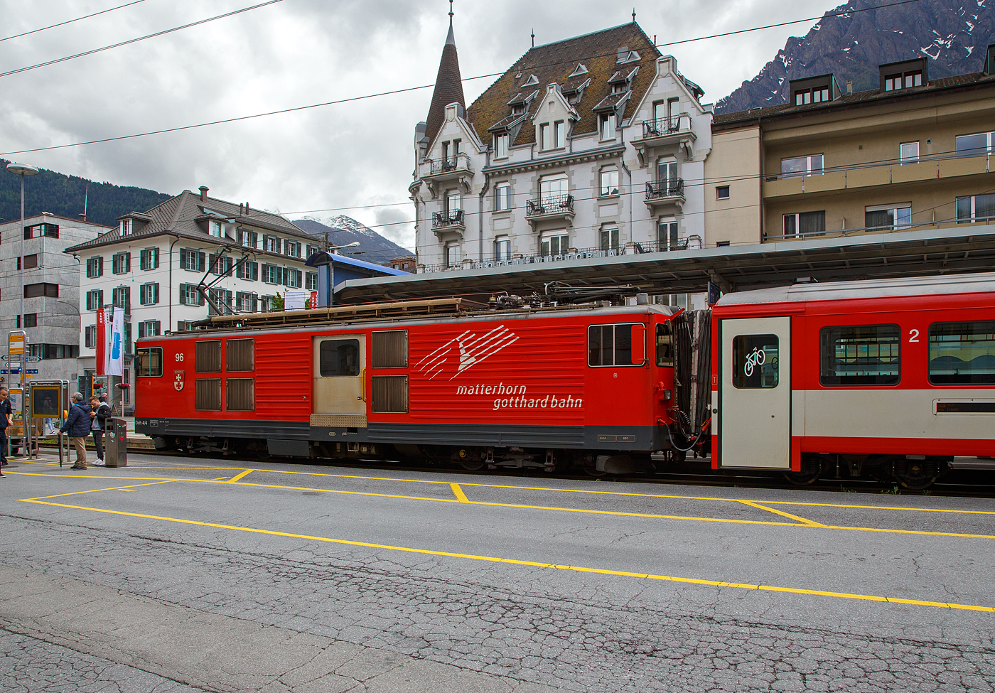 Der Gepäcktriebwagen Deh 4/4 II - 96  Münster   der Matterhorn-Gotthard-Bahn (MGB), ex FO 96  Münster   (Furka-Oberalp-Bahn), am 25.05.2023 mit einen Regionalzug von Andermatt nach Visp im Bahnhof (Vorplatz) Brig.

Der Elektrischer Zahnradtriebwagen wurde 1984 von SLM (mechanischer Teil, Lokomotivkasten) und BBC (elektrische Ausrüstung) gebaut.

Die vier 1980 bei der Furka- Oberalp-Bahn in Betrieb genommenen Gepäcktriebwagen sind für Adhäsions- und Zahnstangenstrecken konzipiert. Zwei weitere Einheiten wurden 1982 in Auftrag gegeben. Sie werden auf dem ganzen Streckennetz – maximale Steigung 179%o - als Triebfahrzeuge für Züge mit vier bis fünf Wagen eingesetzt. Der biege- und verwindungssteife, extrem leichte Kasten wurde in Stahl ausgeführt und die hohe Steifigkeit durch Strukturgebung erzielt. Dem leichten Innenausbau und der ergonomischen Führerstandgestaltung wurde ebenfalls besondere Aufmerksamkeit geschenkt.

Die Drehgestelle, die durch tiefliegende Drehzapfen über Traversen  mit dem Kasten verbunden sind, enthalten je zwei Antriebsmotoren. Die Betriebsverhältnisse erfordern drei unabhängige Bremssysteme.

Die ehemaligen Deh 4/4 I und II der FO (Furka-Oberalp-Bahn) werden im Einsatz nicht unterschieden, wenn nötig, dann anhand der Seriennummern 2.., 5.. und 9... Wobei sie sich optisch und technisch schon etwas unterscheiden. Sie werden hauptsächlich zusammen mit zwei Mittelwagen und einem Steuerwagen als fest gekuppelte Pendelzüge eingesetzt. Zwischen Disentis und Andermatt (Oberalp, 110‰) kann ein und zwischen Visp und Andermatt (Goms, 90‰) können zwei, im Sommer drei Verstärkungswagen angehängt werden. Zwischen Andermatt und Göschenen (Schöllenenschlucht, 179‰) sind keine Verstärkungswagen möglich. Die Pendelzüge sind innerhalb der Komposition mit der automatischen +GF+-Kupplung (GFN) verbunden. Für andere Verwendungen müssen die Kupplungen getauscht werden. Mindestens ein Triebwagen, früher waren dies meist Nr. 95 oder 96, dient als Ersatzfahrzeug für die übrigen Deh und wird auch allein für Überfuhren eingesetzt. Früher wurden auch Güterzüge nach Göschenen geführt.

TECHNISCHE DATEN:
Spurweite: 1.000 mm
Achsformel: Bo’Bo’
Länge über Puffer: 15.500 mm
Drehzapfenabstand: 8.800 mm
Achsabstand im Drehgestell: 2.790 mm
Größte Breite: 2.683 mm
Größte Höhe (bei abgesenkten Stromabnehmer): 3.880 mm
Leergewicht: 49,5 t (davon Mechanischer Teil 28 ,5 t)
Dienstgewicht: 51,0 t
Maximale Zuladung: 1,5 t
Gepäckraum Fläche: 10 m²
Höchstgeschwindigkeit: Adhäsion 60 km/h / Zahnstange 30 km/h
Stundenleistung: 1.032 kW
Dauerleistung: 936 kW
Stundenzugkraft am Rad: 117,2 kN
Dauerzugkraft am Rad: 101,2 kN
Maximale Zugkraft am Rad: 247,2 kN
Stromsystem: 11 kV 16,7 Hz AC
Anzahl der Fahrmotoren: 4