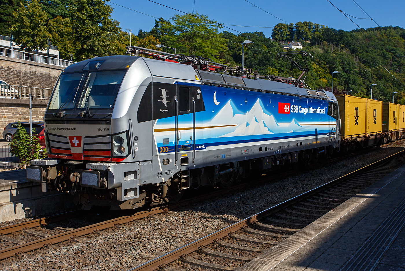 Die an die SBB Cargo International AG vermietete Siemens Vectron MS - 193 110  Zugersee  (91 80 6193 110-4 D-Rpool) der Railpool GmbH (München) fährt am 18 August 2025 mit einem Containerzug durch den Bahnhof Kirchen/Sieg in Richtung Siegen. 

Die SIEMENS Vectron MS (X4E) wurde 2023 von Siemens Mobility in München-Allach unter der Fabriknummer 23293 gebaut. Die mit 6.400 kW konzipierte Mehrsystemlok ist in der Variante A22 ausgeführt und hat so die und hat so die Zulassungen und entspr. Länderpakete für Deutschland, Österreich, Schweiz, Italien und die Niederlande (D / A / CH / I / NL), wobei z.Z. CH und I noch durchgestrichen sind. Sie ist die 300th Lokomotive der Railpool. 