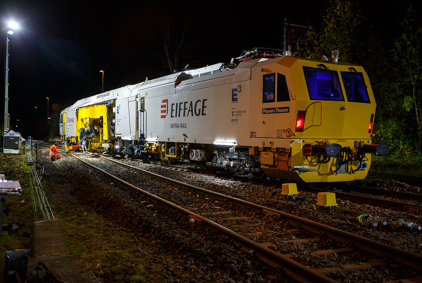 Die Baustelle Bahnhof Herdorf am Abend des 26 Oktober 2025, nun ab 20:40 Uhr wird die neue Weiche 3, beim Bahnhof/Stellwerk Herdorf Fahrdienstleiter (Hf), gestopft. Hier kam die recht neue Plasser & Theurer UNIMAT 09-4x4/4S E³ (A-PLA 99 81 9124 004-8), eine Universal-Weichenstopfmaschine mit Hybrid-Antriebstechnik, der Firma Eiffage Infra-Rail GmbH (Herne) zum Einsatz. Ob die Maschine nur von Eiffage Infra-Rail gemietet oder nun gekaut wurde ist mir nicht klar, aber eingestellt ist sie in Österreich über Franz Plasser Vermietung von Bahnbaumaschinen GmbH. 
Die Maschine wurde 2017 von Plasser & Theurer in Linz unter der Fabriknummer 6557/58 gebaut. Diese Maschine mit der neuen E³-Antriebstechnologie von Plasser & Theurer wurde erstmals 2017 auf der iaf 2017 in Münster präsentiert, wo ich sie am 01.06.2017 auch ablichten und sogar in ihr Platz nehmen konnte. Siehe u.a.:
http://hellertal.startbilder.de/bild/oesterreich~bahndienstfahrzeuge~stopfmaschinen/572409/neues-maschinendesign-und-neue-e179-antriebstechnologie-von.html
und
http://hellertal.startbilder.de/bild/oesterreich~bahndienstfahrzeuge~stopfmaschinen/572406/der-blick-des-maschinenfuehrers-auf-das.html
Leider ist die Helltalbahn nicht elektrifiziert, somit konnte die Maschine den Bahnhof Herdorf nur mit Dieselantrieb (diesel-elektrisch) anfahren und nur im Dieselbetrieb arbeiten. Wenn aber eine Oberleitung vorhanden ist, dann kann die Maschine auch rein elektrisch arbeiten. 
Die Fahrantriebe sind elektrisch im Dieselbetrieb diesel-elektrisch. Im Arbeitsmodus werden alle Drehbewegungen elektrisch, Linearbewegungen hydraulisch. Zudem wir im Dieselbetrieb überschüssige elektrische Energie ins Netz zurück gespeist. 
Der diesel-elektrisch angetriebener Fahrmodus und Arbeitsmodus:
Ein Dieselmotor mit einer Leistung von 600 kW liefert die Energie für die elektrische Versorgung der Antriebskomponenten über den Trafo und Stromrichter. Er wirkt dabei als Generator. Im Arbeitsbetrieb funktionieren die Aggregate gleichermaßen wie im elektrischen Modus. Wichtigster Vorteil ist die Reduktion von der CO2-Emission und von Lärm (10 dBA Lärmreduzierung). Weniger Triebstoffverbrauch, höhere Energieeffizienz im Diesel-elektrischen Betrieb. Ich konnte persönlich feststellen, dass die Maschine (auch beim Stopfen) erheblich leiser ist, als andere klassische Maschinen. 
TECHNISCHE DATEN:
Fahrzeugbegrenzungsprofil: G1
Spurweite: 1.435 mm (Normalspur)
Anzahl der Achsen: 8 (in 4 Drehgesten)
Länge über Puffer:  34.140 mm
Drehzapfenabstände: 11.250 mm / 4.550 mm / 10.300 mm
Achsabstand im Drehgestell: 1.800 mm
Raddurchmesser (neu): 920 mm
Eigengewicht: 142.000 kg
Kleister befahrbarer Gleisbogen: R = 150 m 
Zugelassen für Streckenklasse: C2 und höher
Höchstgeschwindigkeit: 100 km (eigen und geschleppt)
Kraftstofftank: max. 2.580 l (Diesel)
Wirkungsgrad: bis zu 94 %
Bremse:2 x KE-GP mZ (K)
Bremssohle: J 816 M Die Baustelle Bahnhof Herdorf am Abend des 26 Oktober 2025, nun ab 20:40 Uhr wird die neue Weiche 3, beim Bahnhof/Stellwerk Herdorf Fahrdienstleiter (Hf), gestopft. Hier kam die recht neue Plasser & Theurer UNIMAT 09-4x4/4S E³ (A-PLA 99 81 9124 004-8), eine Universal-Weichenstopfmaschine mit Hybrid-Antriebstechnik, der Firma Eiffage Infra-Rail GmbH (Herne) zum Einsatz. Ob die Maschine nur von Eiffage Infra-Rail gemietet oder nun gekaut wurde ist mir nicht klar, aber eingestellt ist sie in Österreich über Franz Plasser Vermietung von Bahnbaumaschinen GmbH. 
Die Maschine wurde 2017 von Plasser & Theurer in Linz unter der Fabriknummer 6557/58 gebaut. Diese Maschine mit der neuen E³-Antriebstechnologie von Plasser & Theurer wurde erstmals 2017 auf der iaf 2017 in Münster präsentiert, wo ich sie am 01.06.2017 auch ablichten und sogar in ihr Platz nehmen konnte. Siehe u.a.:
http://hellertal.startbilder.de/bild/oesterreich~bahndienstfahrzeuge~stopfmaschinen/572409/neues-maschinendesign-und-neue-e179-antriebstechnologie-von.html
und
http://hellertal.startbilder.de/bild/oesterreich~bahndienstfahrzeuge~stopfmaschinen/572406/der-blick-des-maschinenfuehrers-auf-das.html
Leider ist die Helltalbahn nicht elektrifiziert, somit konnte die Maschine den Bahnhof Herdorf nur mit Dieselantrieb (diesel-elektrisch) anfahren und nur im Dieselbetrieb arbeiten. Wenn aber eine Oberleitung vorhanden ist, dann kann die Maschine auch rein elektrisch arbeiten. 
Die Fahrantriebe sind elektrisch im Dieselbetrieb diesel-elektrisch. Im Arbeitsmodus werden alle Drehbewegungen elektrisch, Linearbewegungen hydraulisch. Zudem wir im Dieselbetrieb überschüssige elektrische Energie ins Netz zurück gespeist. 
Der diesel-elektrisch angetriebener Fahrmodus und Arbeitsmodus:
Ein Dieselmotor mit einer Leistung von 600 kW liefert die Energie für die elektrische Versorgung der Antriebskomponenten über den Trafo und Stromrichter. Er wirkt dabei als Generator. Im Arbeitsbetrieb funktionieren die Aggregate gleichermaßen wie im elektrischen Modus. Wichtigster Vorteil ist die Reduktion von der CO2-Emission und von Lärm (10 dBA Lärmreduzierung). Weniger Triebstoffverbrauch, höhere Energieeffizienz im Diesel-elektrischen Betrieb. Ich konnte persönlich feststellen, dass die Maschine (auch beim Stopfen) erheblich leiser ist, als andere klassische Maschinen. 
TECHNISCHE DATEN:
Fahrzeugbegrenzungsprofil: G1
Spurweite: 1.435 mm (Normalspur)
Anzahl der Achsen: 8 (in 4 Drehgesten)
Länge über Puffer:  34.140 mm
Drehzapfenabstände: 11.250 mm / 4.550 mm / 10.300 mm
Achsabstand im Drehgestell: 1.800 mm
Raddurchmesser (neu): 920 mm
Eigengewicht: 142.000 kg
Kleister befahrbarer Gleisbogen: R = 150 m 
Zugelassen für Streckenklasse: C2 und höher
Höchstgeschwindigkeit: 100 km (eigen und geschleppt)
Kraftstofftank: max. 2.580 l (Diesel)
Wirkungsgrad: bis zu 94 %
Bremse:2 x KE-GP mZ (K)
Bremssohle: J 816 M
