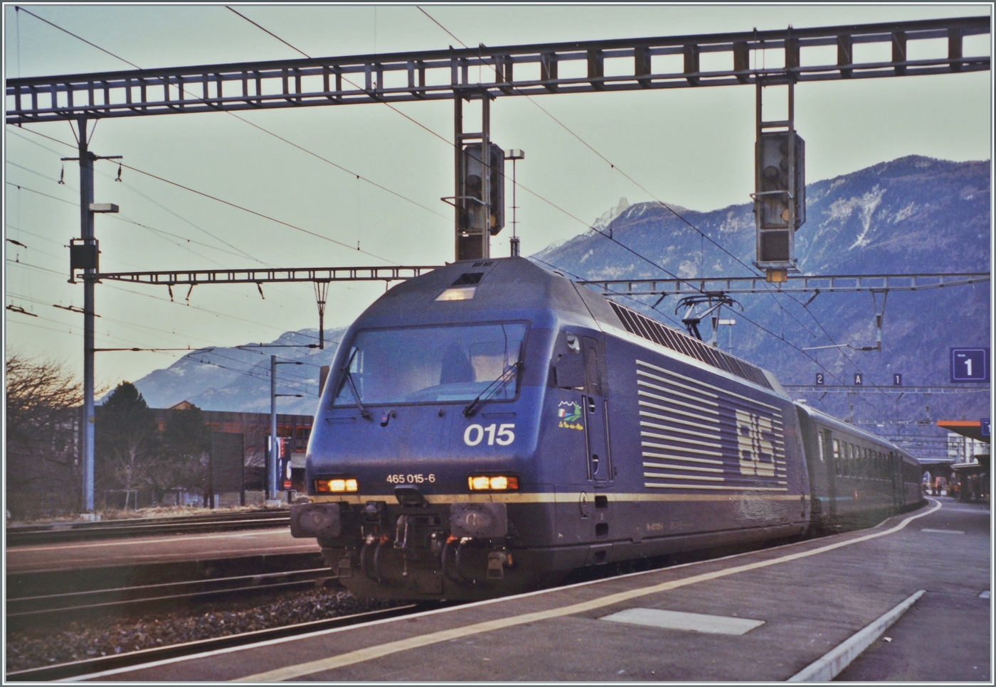 Die BLS Re 465 015-6 mit einem Schnellzug in Richtung Lausanne beim Halt in Martigny. 

Analogbild vom 10. Februar 2000