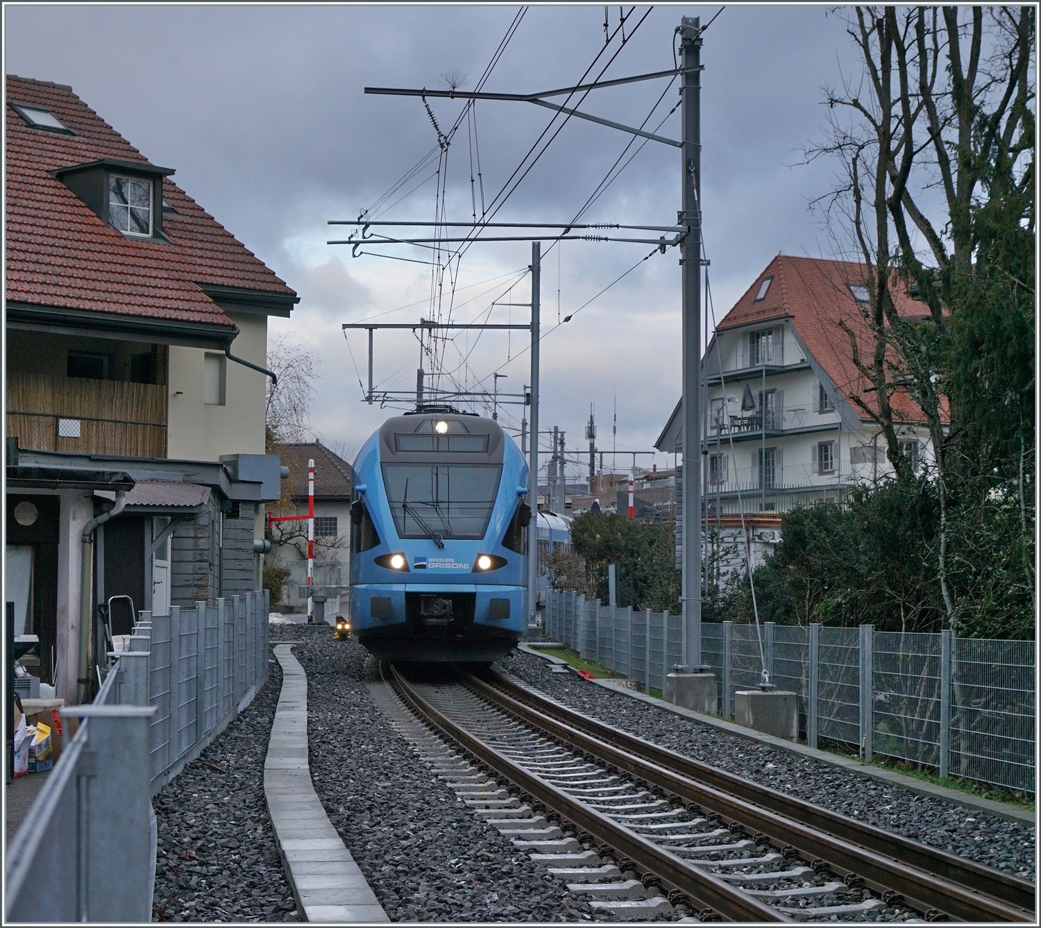 Die gut 700 Meter lange Strecke des Dreischiengeleis der TPF ist meist nur bei Bahnübergängen zugänglich und führt durch ein recht dicht bebautes Stadtgebiet von Bulle. Da über die Strecke zwei Zugspaare pro Stunde verkehren gibt acht Züge pro Stunde, Normal- und Schmalspurzüge folgen bisweilen auf Blockdistanz. 

Im Bild ist der normalspurige TPF RABe 527 198  Groupe Grisoni  und der nicht zu sehende RABe 527 192 als RE 3812 von Bern nach Broc Village kurz nach der Abfahrt in Bulle unterwegs. 22. Dezember 2022 