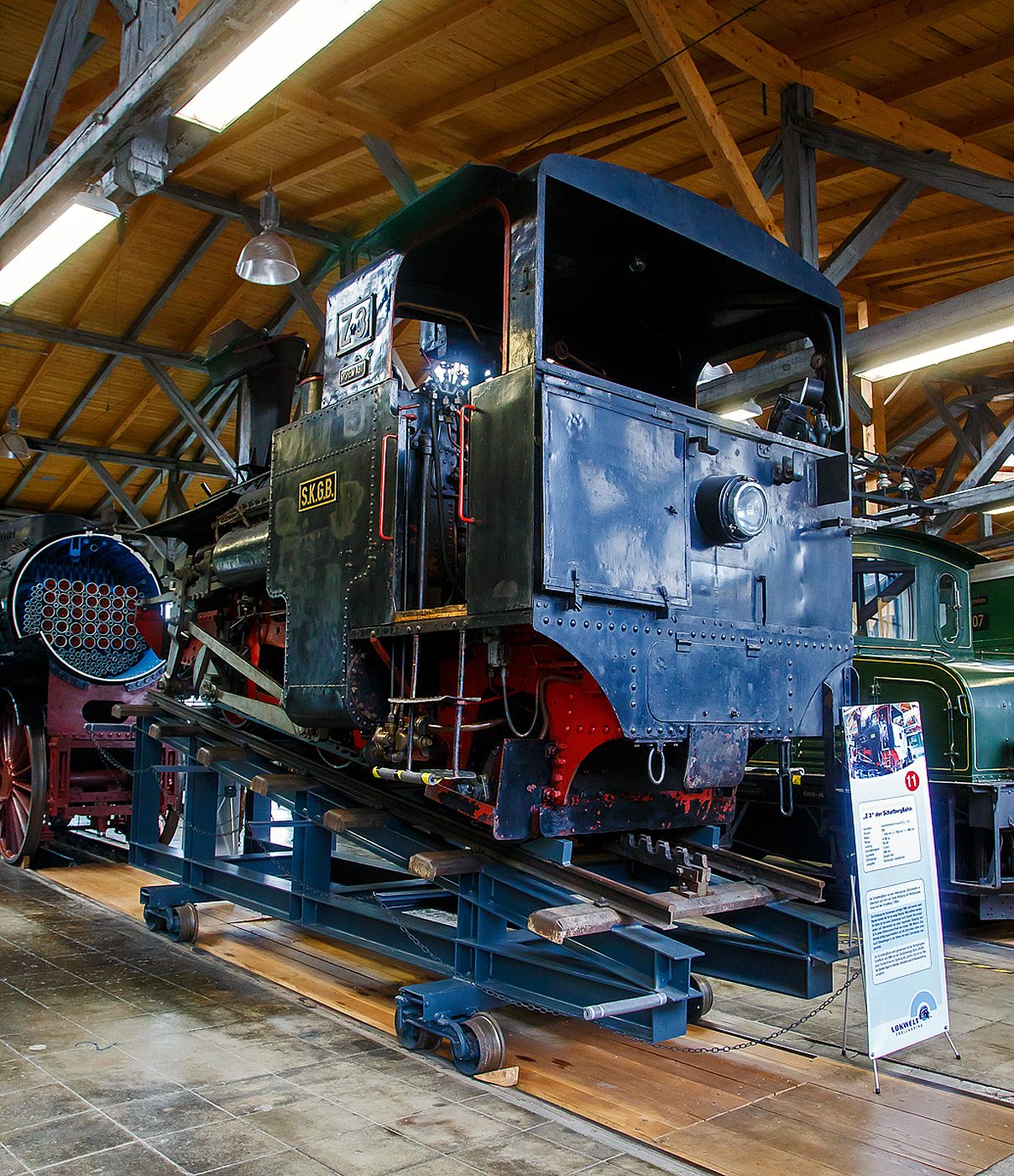 Die kohlegefeuerte Zahnraddampflokomotive SKGLB Z3 „Erika“ der Schafbergbahn, ex SKGB 999.103 „Erika“, ex BB Z3, ex BB 999.103 „Erika“ am 11.09.2022 in der Lokwelt Freilassing.

Die Lok wurde 1893 von der Lokomotivfabrik Krauss & Comp. In Linz unter der Fabriknummer 2746 gebaut und an die Salzkammergut-Localbahn-Actiengesellschaft (SKGLB) fr die Zahnradbahn auf den Schafberg geliefert. Die Lok ist Eigentum der Salzkammergutbahn GmbH und wurde 2007 als Leihgabe in die „Lokwelt Freilassing“ abgegeben.

Die Dampflokomotiven SKGLB Z sind eine Schmalspur-Zahnrad-Tenderlokomotivreihe der Bauart Abt (H 2/3), von denen ursprnglich sechs Loks Krauss in Linz (abgeleitet der Bauart H 2/3 der Schweizerischen Lokomotiv- und Maschinenfabrik Winterthur) fr die Schafbergbahn der Salzkammergut-Lokalbahn (SKGLB) gebaut wurden. Eine weitgehend baugleiche Serie von Loks wurde 1896/1900 von der Schneebergbahn-Gesellschaft (SchBB) beschafft. Von den spter zu den sterreichischen Bundesbahnen gehrenden Lokomotiven sind heute noch vier Stck betriebsfhig. Die Maschinen sind aufgrund der Steigung stark geneigt, damit der Kessel whrend der Fahrt in der Ebene liegt. Die Kesselneigung ist der einzige nennenswerte Unterschied zwischen den beiden Baureihen und betrgt bei den am Schafberg eingesetzten Maschinen 170 ‰, bei den Lokomotiven der Schneebergbahn 120 ‰. Die Lokomotiven besitzen einen Auenrahmen, der im Bereich der Nachlaufachse zu einem Innenrahmen verengt wird.

Der Antrieb erfolgt von einem obenliegenden und relativ kurzhubigen Zylinder (System Brown) ber einen Balancierhebel und Treibstangen auf die beiden gekuppelten Zahnradachsen. Die Leistung betrgt ungefhr 200 PS. Die Steuerung erfolgt ber eine innenliegende Exzentersteuerung System Gooch. Es werden lediglich die beiden Zahnrder angetrieben, die Rder sind lediglich lose mitdrehend und dienen ausschlielich der Fhrung im Gleis. Deshalb mssen auch die ebenen Streckenabschnitte mit Zahnstangen ausgerstet sein.

Die Lokomotiven werden mit Kohle gefeuert. 1954/55 erhielten die Maschinen einen Giesl-Ejektor mit Mikrofunkenfnger. Der Wasserkasten fasst 1,2 m. Zustzlich werden ca. 300 Liter zur Khlung der Zylinder bei der Talfahrt mitgefhrt.

Gebremst wird ber eine Gegendruckbremse Bauart Riggenbach sowie eine Rillen-Bandbremse. In den 1960er Jahren wurden die Lokomotiven mit einer bei berschreitung der Hchstgeschwindigkeit automatisch auslsenden Notbremse in Form einer als Bandbremse ausgefhrten Druckluftbremse ausgerstet. Da jedoch auf den kleinen Lokomotiven kein Platz fr einen Druckluftpumpe und einen Luftbehlter war, wurden Druckluftflaschen an den Fhrerhaus-Rckwnden montiert.

TECHNISCHE DATEN:
Gebaute Anzahl: 6 (Schafbergbahn) / 5 (Schneebergbahn)
Hersteller:  Krauss & Comp./Linz
Baujahre: 1893, 1896–1900
Spurweite:  1.000 mm (Meterspur)
Achsformel: 2zz1'  n2t
Lnge ber Puffer:  4.545 mm
Hhe: 3.300 m
Eigengewicht: 14,5 t
Hchstgeschwindigkeit: 12 km/h
Zahnrad-Teilkreis- (Treibrad): 573 mm
Laufraddurchmesser vorn: 706 mm
Laufraddurchmesser hinten: 520 mm
Zahnradsystem:  Abt
Steuerungsart: Exzentersteuerung
Zylinder: 2 x  320 mm x 600 mm Hub
Kesselberdruck: 14,0 bar
Leistung (ca.): 150 kW (200 PS)
Anzahl der Heizrohre: 150
Heizrohrlnge: 2.000 mm
Rostflche: 0,9 m
Wasservorrat: 1,2 m
Kohlevorrat: 0,6 t
Lokbremse: Rillenband-, Riggenbach-Gegendruckbremse
Max. Steigung: 255‰ (Schafbergbahn), 197‰ (Schneebergbahn)
Besonderheiten:  Giesl-Ejektor

Die Schafbergbahn ist eine meterspurige reine Zahnradbahn (System Abt) in sterreich. Sie verkehrt zwischen St. Wolfgang am Wolfgangsee  (542 m .M.) und dem Schafberg (1.782 m .M.). Die Talstation liegt in Obersterreich, die Bergstation im Bundesland Salzburg. Die Bahn ist mit einer Zahnstange nach System Abt ausgestattet und berwindet bei einer maximalen Steigung von 255 ‰ einen Hhenunterschied von 1.190 Metern. Der Antrieb erfolgt ausschlielich durch die Zahnrder, daher sind auch waagrechte und wenig geneigte Gleise mit einer Zahnstange ausgerstet. Die Strecke ist nicht elektrifiziert und wird von Dampf- und Dieselloks befahren. Von den historischen Originalmaschinen der Type SKGLB Z (Baujahre 1893/1894) sind noch drei Exemplare, bei der Schafbergbahn vorhanden, diese kommen im Zuge eines eigenen Nostalgiefahrplanes zum Einsatz. Mit ihnen betrgt die Fahrzeit zum Gipfel eine Stunde statt 35 Minuten.

Die Schafbergbahn wurde 1932 an das sterreichische Verkehrsbro verkauft. 1938 ging sie an die Deutsche Reichsbahn und somit nach dem Zweiten Weltkrieg an die BB ber. Seit 2006 betreibt die Salzkammergutbahn GmbH (SKGB), eine Tochterfirma der Salzburg AG, die Schafbergbahn und die Wolfgangseeschifffahrt.
