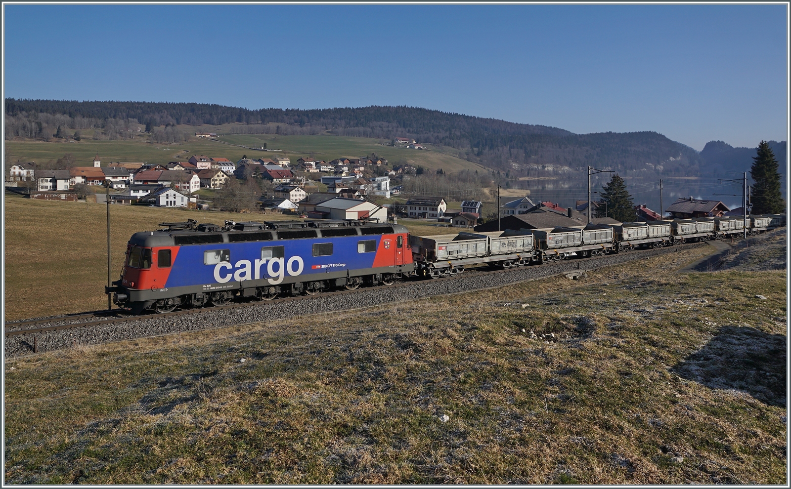 Die SBB Re 6/6 11610 (Re 620 010-9)  Spreitenbach  bringt etliche leere Fans-u Wagen als Gterzug 69701 von Lausanne-Triage nach Le Brassus und konnte hier bei Les Charbonnires mit dem Hintergrund des Lac de Brenet fotografiert werden. 24. Mrz 2022