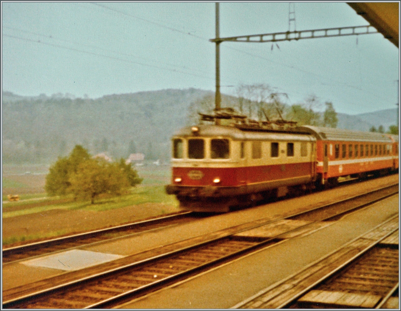 Eine SBB Re 4/4 I ist mit einem Schnellzug von Bern nach Paris auf dem Weg nach Pontarlier und fährt durch den Bahnhof von Gümmenen. 

Analogbild vom 3. Mai 1981