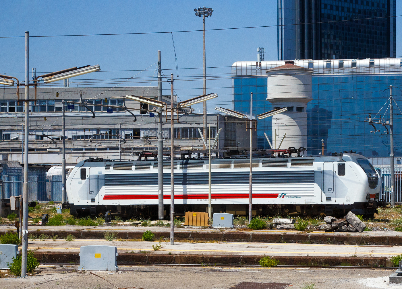 Eine Trenitalia E.403 (91 83 2402 0xx-8 I-TI), in weiß-grau-roter IC-Lackierung, ist am 16.07.2022 beim Bahnhof Napoli Centrale abgestellt. Die Aufnahme konnte ich aus einem ausfahrenden IC machen.

Die Trenitalia / FS E.403 baut auf die FS E.402B auf, war auch ursprünglich als E.402 C vorgesehen, haben aber einen anderen elektrischen und elektronischen Teil als die E.402B. 24 Loks wurden von AnsaldoBreda zwischen 2005 bis 2008 gebaut. 

Anfang der 2000er Jahre entwickelte Trenitalia Pläne zur Ausweitung seines Güterverkehrs auf das europäische Festland, insbesondere auf dem Korridor Italien-Österreich-Deutschland sowie der Schweiz. 
Eine neue Lokomotive musste konzipiert werden, damit die Pläne Wirklichkeit werden konnten, und wurde ursprünglich als E.402C bezeichnet. Es war eine Weiterentwicklung der E.402B-Lokomotive mit zusätzlicher Ausrüstung für den Betrieb in diesen Ländern und wesentlich anderen Hembot-Drehgestellen. Die Loks waren für den Einsatz vor schnellen Güterzügen vorgesehen und hatten ursprünglich auch vier Einholm-Stromabnehmer für Oberleitungen-Spannungen von 1,5 kV DC, 3 kV DC, 15 kV ~ 16 2/3 Hz und 25 kV ~ 50 Hz. 

Das Programm erlitt große Schläge: Als AnsaldoBreda diese Lokomotivenserie exklusiv für Trenitalia auf einer nicht standardmäßigen Plattform (im Gegensatz zu den Lokomotiven der TRAXX und EuroSprinter/Vectron, die sich Standardkomponenten teilen) baute, explodierten die Kosten. Die Lokomotive wurde verkleinert, indem die 1,5-kV- und 15-kV-Teile sowie die französischen, deutschen und österreichischen Sicherheitssysteme entfernt wurden. Stattdessen übernahm Trenitalia 51% der Anteile an TXLogistik und beantragte die Zulassung seiner E.412- Lokomotiven in Österreich und Deutschland. Die (eingeschränkte) österreichische und deutsche Zulassung wurde 2006 erteilt, wobei TXLogistik Lokführer die Züge in Österreich und Deutschland fahren.


Die Lokomotive sollte nun in schnellen Güterzügen eingesetzt werden, die teilweise auf den neuen Hochgeschwindigkeitsstrecken verkehren. Bis Februar 2010 verkehrte jedoch noch kein Güterzug auf den HS-Strecken und die E.403 waren noch nicht im Linienverkehr. In den ersten Monaten des Jahres 2010 beschloss die Trenitalia, diese Lokomotiven der Passagierabteilung zuzuordnen und erst 2012 erfolgte die endgültige Zulassung der Loks.

Aus der Mehrsystemlokomotive wurde eine rein italienische Zweisystemlokomotive für 3 kV Gleich- und 25 kV 50 Hz~ Wechselstrom. Die Baureihe E.403 kann so unter 3.000 V Gleichstromspannung, dem hauptsächlichen italienischen Bahnnetz, aber auch auf den italienischen Schnellfahrstrecken mit 25 kV, 50 Hz Wechselstrom fahren. Fernerhin kann sie unter 1.500 V Gleichstrom betrieben werden, dann hat sie aber nur die halbe Leistung. Die Lokomotiven verfügen über eine elektrische regenerative und rheostatische Bremse, sowie eine mechanische Scheibenbremse mit zwei Scheiben pro Achse. Die Loks haben auch ein variables Übersetzungsverhältnis von 45/71 oder 33/92. 

TECHNISCHE DATEN:
Hersteller: AnsaldoBreda
Gebaute Anzahl: 24 
Baujahre: 2005-2008 (Ineinssetzung 2012)
Spurweite:  1435 mm (Normalspur)
Achsformel: Bo'Bo'
Länge: 19.900 mm
Drehzapfenabstand: 10.450 mm
Achsabstand im Drehgestell: 2.750 mm
Treibraddurchmesser:  1.110 mm (neu)
Dienstgewicht: 86 t
Höchstgeschwindigkeit: 180 km/h
Übersetzungsverhältnis: variabel 45/71 oder 33/92
Stundenleistung: 6.000 kW
Dauerleistung: 5.600 kW (7.500 PS)
Anfahrzugkraft: 315 kN
Dauerzugkraft: 265 kN
Stromsysteme: 3000 V DC und 25 kV - 50 Hz AC 