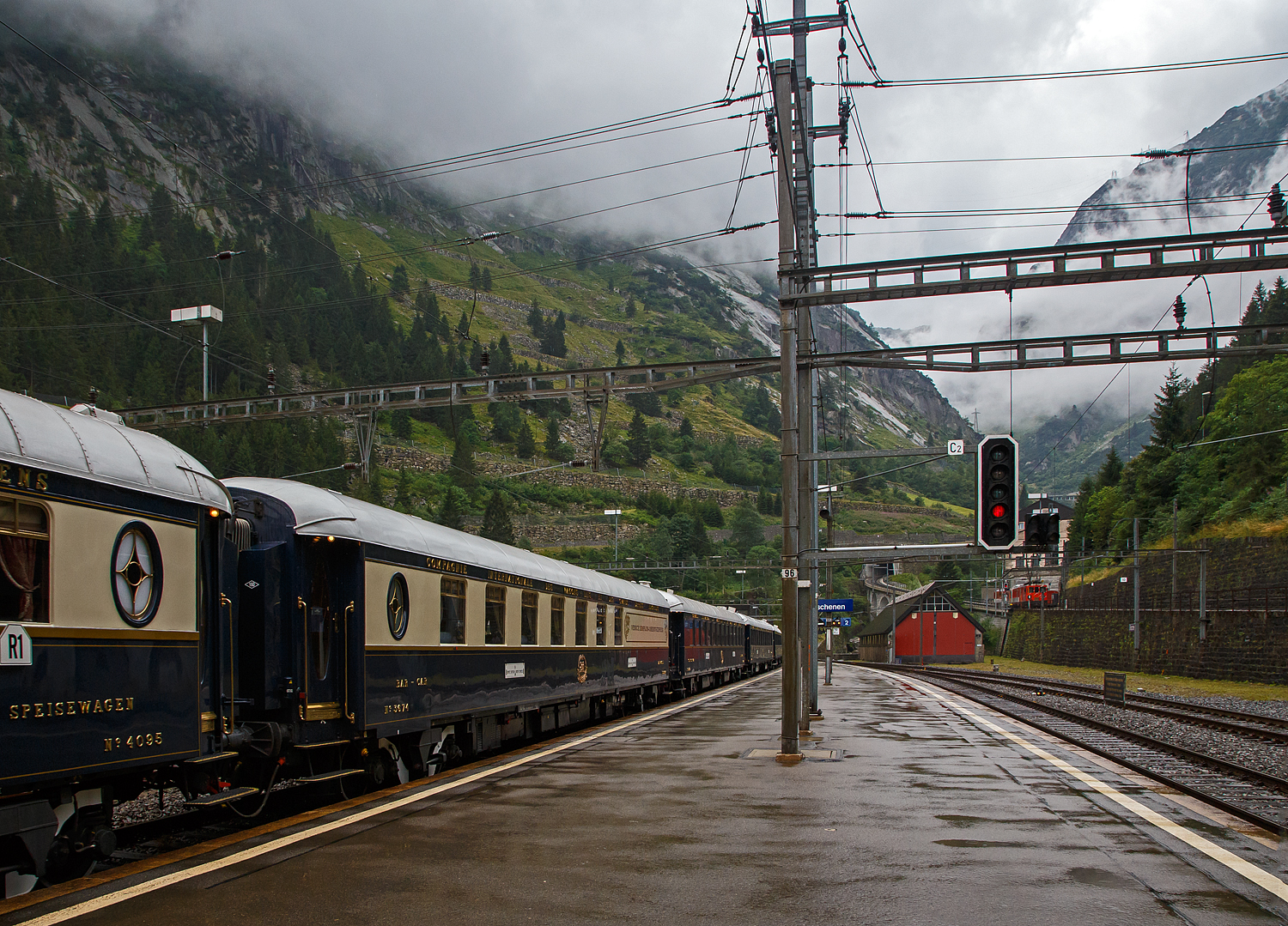 Gezogen von einer SBB Re 8/8 (Doppeltraktion der Re 4/4 11194 und der Re 4/4 11156) verlsst der VSOE - Venice Simplon-Orient-Express von Amsterdam ber Brssel und Paris nach Venedig am 02 August 2019, leider bei Regen, den Bahnhof Gschenen. Hier fhrt er nicht, wie es im Namen steht, durch den Simplon, sondern ber den Gotthard. Der „Knig der Zge“ der Orient-Express, bestand aus einem Zug mit 18 Wagen, es waren modernisierte historische ehemalige CIWL-Wagen. Ob es auch einen „Mord im Orient-Express“ gab? Das kann ich nicht sagen, hatte aber gehrt das man wohl einen im Zug nachspielte.

brigens, rechtshinten kommt gerade der meterspurige Elektrische Zahnradgepcktriebwagen MGB Deh 4 /4 II - 93 „Oberwald“, ex FO Deh 4/4 II – 93, mit seinem Schllenenbahn Regionalzug von Andermatt nach Gschen hinab. Allein dieser wre fr mich schon Bilder wert, aber hier habe ich doch lieber das Augenmerk auf den „Knig“ gehalten😉

Hier im Bild der VSOE (Pullman) Barwagen Nr. 3674, Voiture-Bar / Carrozza-Bar N 3674 (F- VSOE 61 87 09-70 674-0 [P]), ex SNCF WR 51 87 88-40 544-8, ex CIWL N 3674, im Zugverbund vom Venice Simplon-Orient-Express.

Der Barwagen wurde 1931 von EIC - Entreprises industrielles des Charentes in Aytr (F) (EIC, heute zu Alstom gehrend) gebaut und an die CIWL (Compagnie Internationale des Wagons-Lits) geliefert die ihn als Nr. 3674 bezeichnete, damals war es kein Pullman-Wagen. 

Seine Geschichte umfasst den Inlandsverkehr in Frankreich whrend der deutschen Besatzung im 2. Weltkrieg. nach dem Krieg den Sud-Express (Sd-Express) von Paris (Gare d’Austerlitz) ber Orleans-Les Aubrais, Bordeaux (Saint-Jean), Bayonne und Biarritz nach Irun. Irun ist eine spanische Stadt nahe der spanisch-franzsischen Grenze. Ab Irun ging es dann nur breitspurig oder meterspurig weiter. Er lief als WR 51 87 88-40 544-8 der SNCF. 

Ende der 1970er-Jahre wurde er an die VSOE verkauft. Die VSOE lie den ursprnglichen Speisewagen durch die Bremer Waggonbau GmbH (ehem. Hansa Waggonbau) 1982 zum Barwagen umbauen, Innengestaltung erfolgte nach Grard Gallet. Der Wagen wurde sogar mit einem Flgel (Klavier) ausgestattet. Vermutlich erhielt er dort auch an einer Wagenseite ein typisches „Pullman-Fenster“ und wegen der eingebauten Bar an dieser Wagenseite auch einen lngeren fensterlosen Bereich. 

Zwischen 2003 und 2006 wurden die Wagen nochmals modernisiert und erhielten unter anderem moderne Drehgestelle von Bombardier sowie neue Klimaanlagen. Seitdem sind die Wagen nun fr 160 km/h zugelassen.

TECHNISCHE DATEN:
Spurweite: 1.435 mm (Normalspur)
Anzahl der Achsen: 4 in zwei Drehgestellen
Lnge ber Puffer: 23.452 mm
Drehzapfenabstand: 16.000 mm
Achsabstand im Drehgestell: 2.500 mm
Eigengewicht: 49 t
Hchstgeschwindigkeit: 160 km/h (ursprnglich 140 km/h)
Sitzpltze: 36

Nach dem Dinner wird im Barwagen bei sanfter Musik Konversation betrieben. Der Pianist sitzt am Flgel. Es fliet Champagner oder man nippt an Cocktails. Salzgebck wird in Silberschlchen gereicht. Hier wird gelacht. Hier wurden und werden vielleicht immer noch Kontakte geknpft. Wer noch Hunger auf einen Snack versprt, kann sich Blinis mit Beluga-Kaviar anrichten lassen. Einige hundert Euro extra werden dafr am Ende der Tour wohl auf der Rechnung stehen😉. Eine Fahrt im VSOE ist keine „All-inclusive-Reise“, auch wenn viele inclusive ist. 

Schlielich ist die Vorstellung vorbei und man zieht sich ins Abteil zurck. Vielleicht mit der passenden Bettlektre von Agatha Christie, um beim monotonen Klackadiklack der Rder besser einzuschlafen. War da nicht eben ein Schrei? Ist jemand aus dem schaukelnden Bett gefallen? Hat sich jemand im engen Abteil den Kopf gestoen? Doch wieder ein Mord? Traum oder Wirklichkeit? Egal, sptestens wenn man das Frhstck ans Bett serviert bekommt, werden alle erfahren, was in der Nacht im „Knig der Zge“ geschehen ist.
