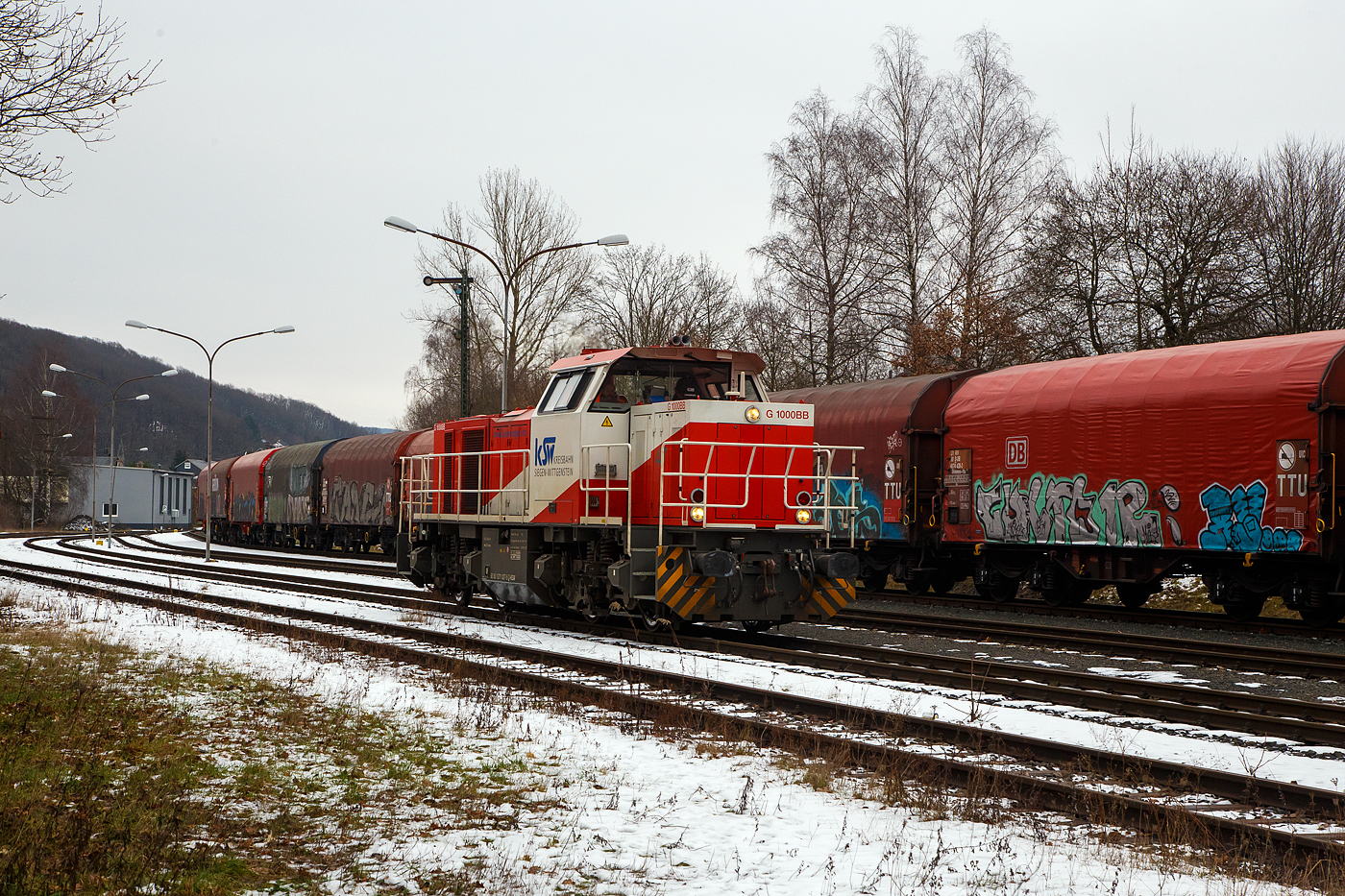 Güterverkehr gibt es noch in Herdorf....
Die KSW 47 (92 80 1271 027-5 D-KSW), ex D 2 der HFM, eine Vossloh G 1000 BB der KSW (Kreisbahn Siegen-Wittgenstein), fährt am 24.01.2023 auf dem KSW Rbf Herdorf (Betriebsstätte Freien Grunder Eisenbahn - NE 447). Gleichdrauf geht es aufs DB Gleis der Hellertalbahn (KBS 462 / Strecke-Nr. 2651). Nur nicht in Richtung Betzdorf, denn der Streckenanschnitt Herdorf – Betzdorf ist bis min. Ende April gesperrt, so muss die KSW den Umweg über Haiger fahren. Wobei hier als Lokzug ist es nur der Umweg und der entsprechende Mehrverbrauch an Kraftstoff, aber für den Güterverkehr ist noch die Streckenklasse sehr entscheidend und die beträgt bei dem Streckenanschnitt Herdorf – Haiger nur CE (anstatt D4 zwischen Betzdorf und Herdorf). Bei CE beträgt die Radsatzlast max. 20 t bei D4 aber 22,5 t. Dadurch kann ein Coil weniger geladen werden, da man nicht gerademal Coils vierteln kann, ergibt sich daraus ein bis zu 35% geringeres Ladegewicht und ein Mehraufwendung von Waggons. 
