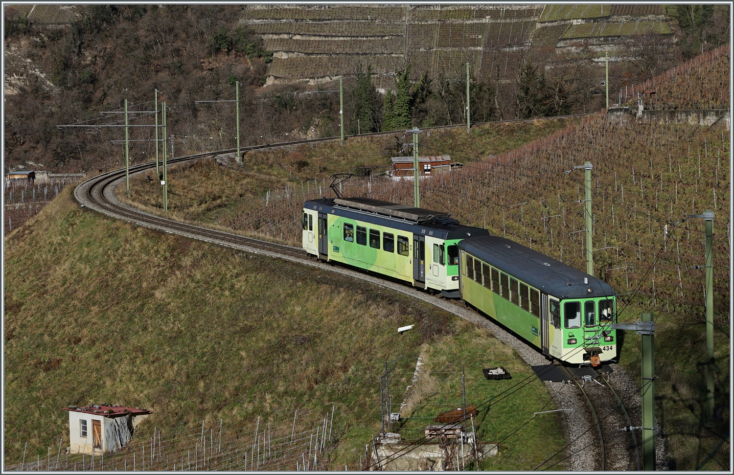 In weiten Schleifen wird das Trasse oberhalb von Aigle durch die Weinberge geführt. Im Bild der Regionalzug R 71 435 von Les Diablerets nach Aigle mit dem schiebenden TPC ASD BDe 4/4 402 und dem Bt 434. Dieser Steuerwagen wurde als Bt 25 bei der BLT in Betrieb genommen, kam dann als Bt 131 zur AOMC, und 2000 nachdem er bei der AOMC nie in Betrieb genommen wurde, zur ASD. Auffällig ist die belassen Stirnwandtür, die dem nun bald sechzig jährigen Bt 434 ein sehr gefälliges Aussehen verleiht. 4. Jan. 2024