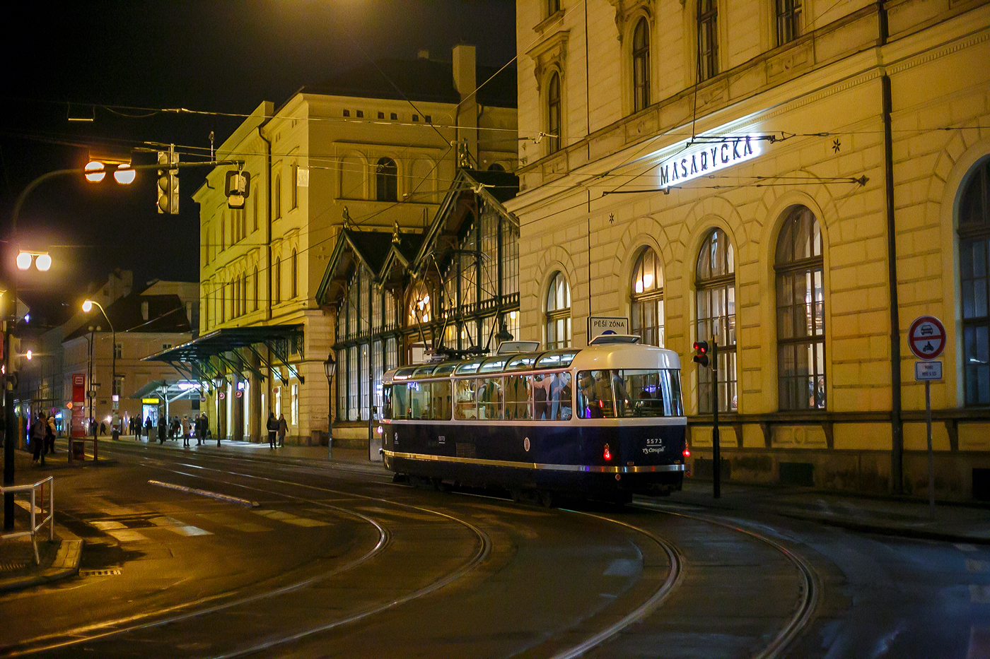 Triebwagen 5573, das T3 Coupé, der Verkehrsgesellschaft der Hauptstadt Prag (DPP - Dopravní podnik hlavního města Prahy a.s.) fährt am Abend des 22.11.2022 über die Havlíčkova beim Bahnhof Praha Masarykovo nádraží vorbei. 

Der Triebwagen vom Typ T3 wurde 1974 von ČKD Tatra in Praha unter der Fabriknummer 162-550 gebaut und als TW 6916 geliefert. In der Prager Hauptwerkstatt UDDP wurde er 2006 zum Typ T3R.P (TW 8497) umgebaut, nach Unfall 2016 wurde er abgestellt. Von CKD Tatra in Praha wurde er 2180 zum Stadtrundfahrtwagen T3 Coupe 5573 umgebaut. So ist er ein Fahrzeug im „Retrodesign“ und kein echter Historischer Wagen.

Praha Masarykovo nádraží ist ein wichtiger Regionalbahnhof und früherer war er auch Fernbahnhof in Prag. Bei diesem Bahnhof befinden auch direkt vor im Straßenbahnhaltestellen (etlicher Linien).
 
Erbaut wurde er in den Jahren 1844/45 im Zuge der k.k. Nördlichen Staatsbahn von Olmütz, welche bis 1851 von Wien nach Dresden durchgehend in Betrieb genommen wurde. Der Bahnhof ist heute der einzige Kopfbahnhof Prags. Er trägt den Namen des ersten Präsidenten der Tschechoslowakei Tomáš Garrigue Masaryk. 

Die ehemaligen Bahnhofsnamen sind:
• 1845–1862 Praha / Prag
• 1862–1919 Praha státní nádraží / Prag Staatsbahnhof
• 1919–1940 Praha Masarykovo nádraží (Prag Masarykbahnhof)
• 1940–1945 Praha Hybernské nádraží / Prag Hibernerbahnhof
• 1945–1952 Praha Masarykovo nádraží
• 1953–1990 Praha střed (Prag Mitte)
• seit März 1990 wieder Praha Masarykovo nádraží
