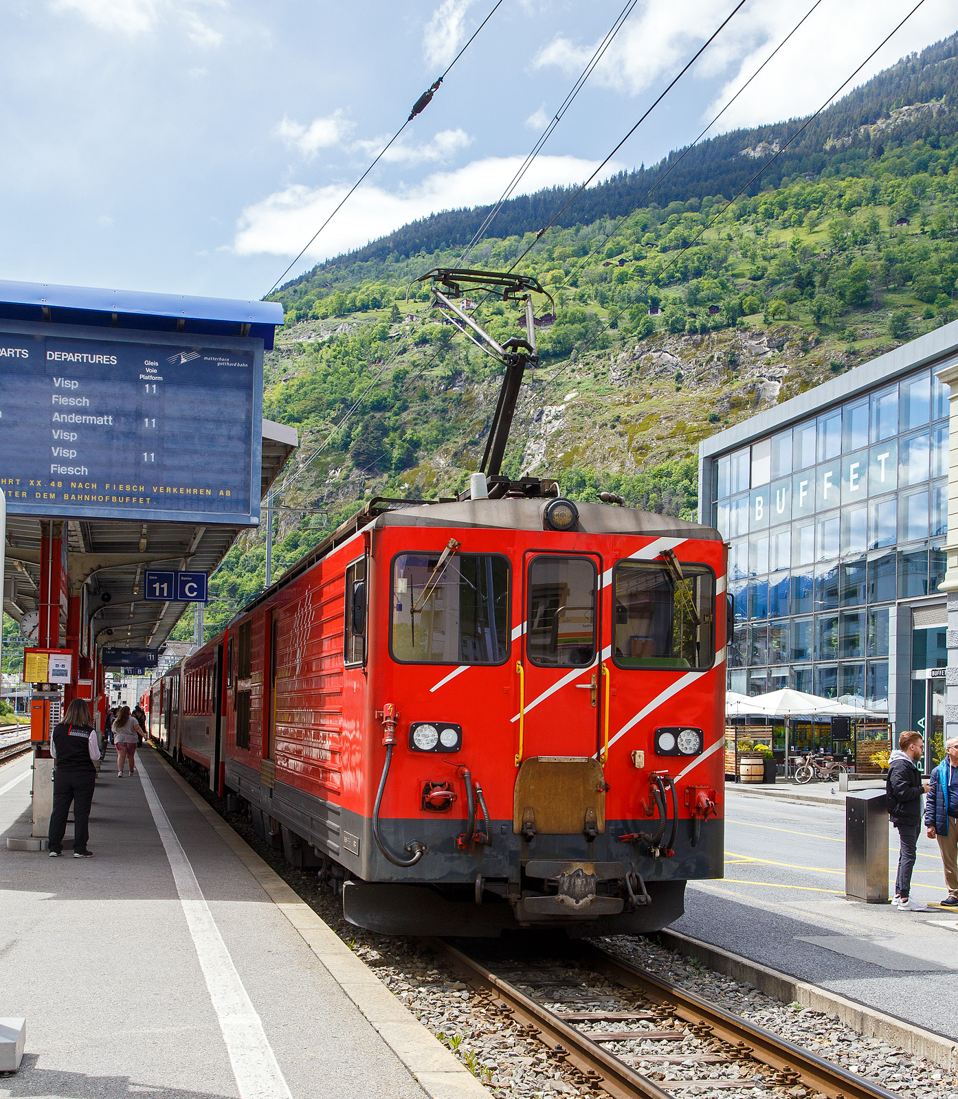Von dem Gepäcktriebwagen Deh 4/4 II - 96  Münster   der Matterhorn-Gotthard-Bahn (MGB), ex FO 96  Münster   (Furka-Oberalp-Bahn), geschoben erreicht am 25.05.2023 der Regionalzug von Andermatt nach Visp den Bahnhof (Vorplatz) Brig.

Der Gepäcktriebwagen wurde 1984 von SLM (mechanischer Teil, Lokomotivkasten) und BBC (elektrische Ausrüstung) gebaut.