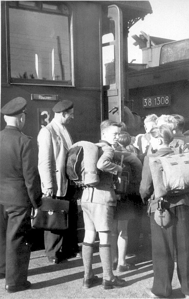 Es ist zu vermuten, dass dieses Foto im Bahnhof Ro�leben entstanden ist. Zuglok des Personenzuges, mit dem Sch�ler und ihr Lehrer verreisen wollen, ist eine ehemalige Preu�ische P8 mit der Reichsbahnnummer 38 1308. Lokomotiven dieser Gattung wurden ab 1906 gebaut. Die 38 1308 war u.a. von 1954 bis 1964 beim Bw Naumburg (S) stationiert. Von dort aus wurden die Lokomotiven vorrangig auf der Unstrutbahn eingesetzt. Da bereits im Jahr 1956 die 3. Wagenklasse bei der DR abgeschafft wurde, k�nnte das Foto etwa 1955 entstanden sein. (Foto zur Verf�gung gestellt von Familie Heidenreich)