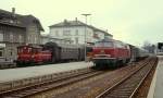 215 005-0 wartet um 1980 vor einem Eilzug nach Ulm im Bahnhof Friedrichshafen Stadt auf Fahrgäste, der Dampf zwischen Lok und Packwagen zeigt, dass die Dampfheizung in Betrieb ist. Links rangiert eine 332 mit einigen Umbau-Vierachsern.